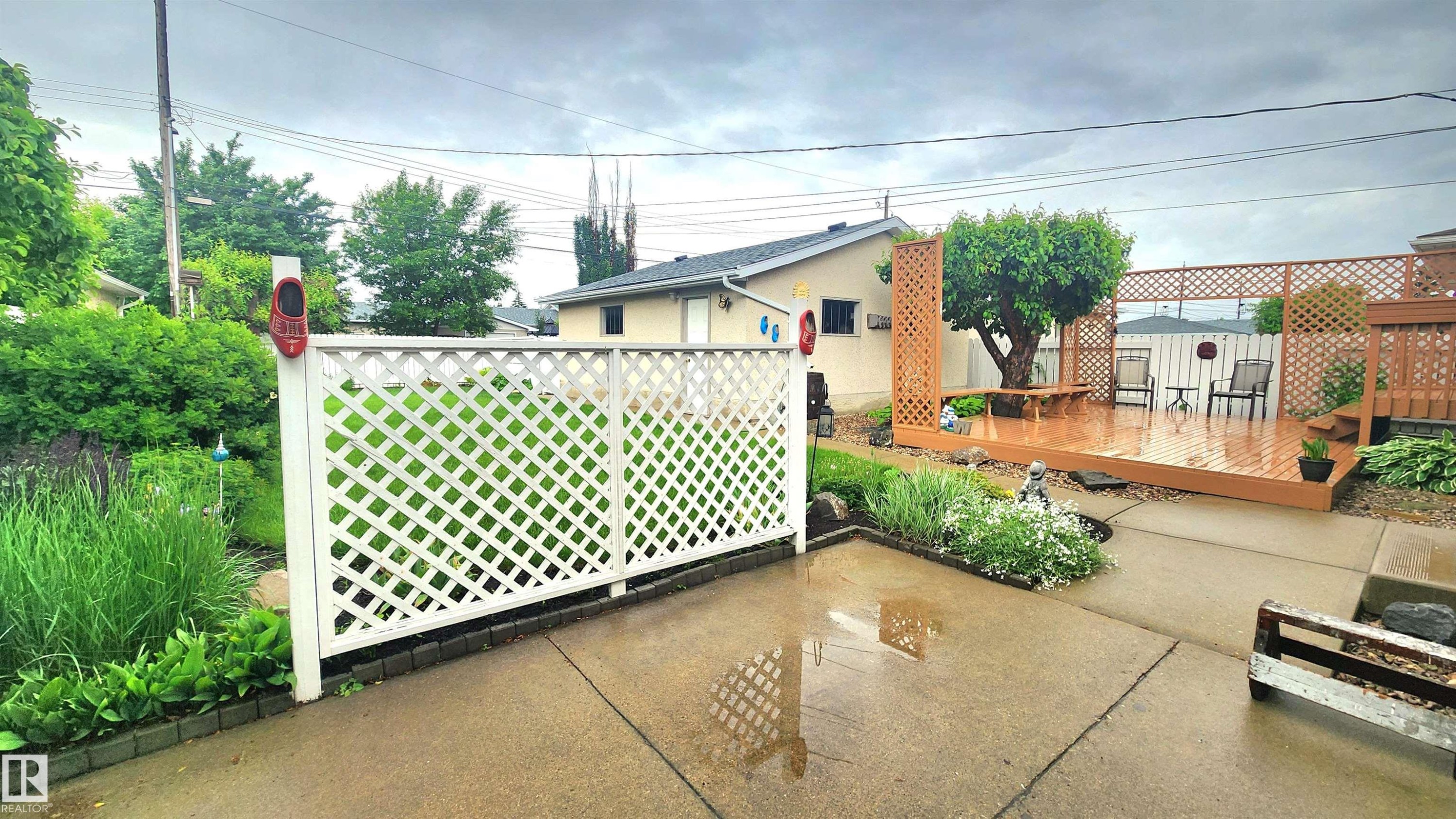 Expansive backyard featuring a multi-level wood deck, white lattice privacy screen, concrete patio, and garden beds with mature plantings - 13307 Delwood Road, Edmonton, AB