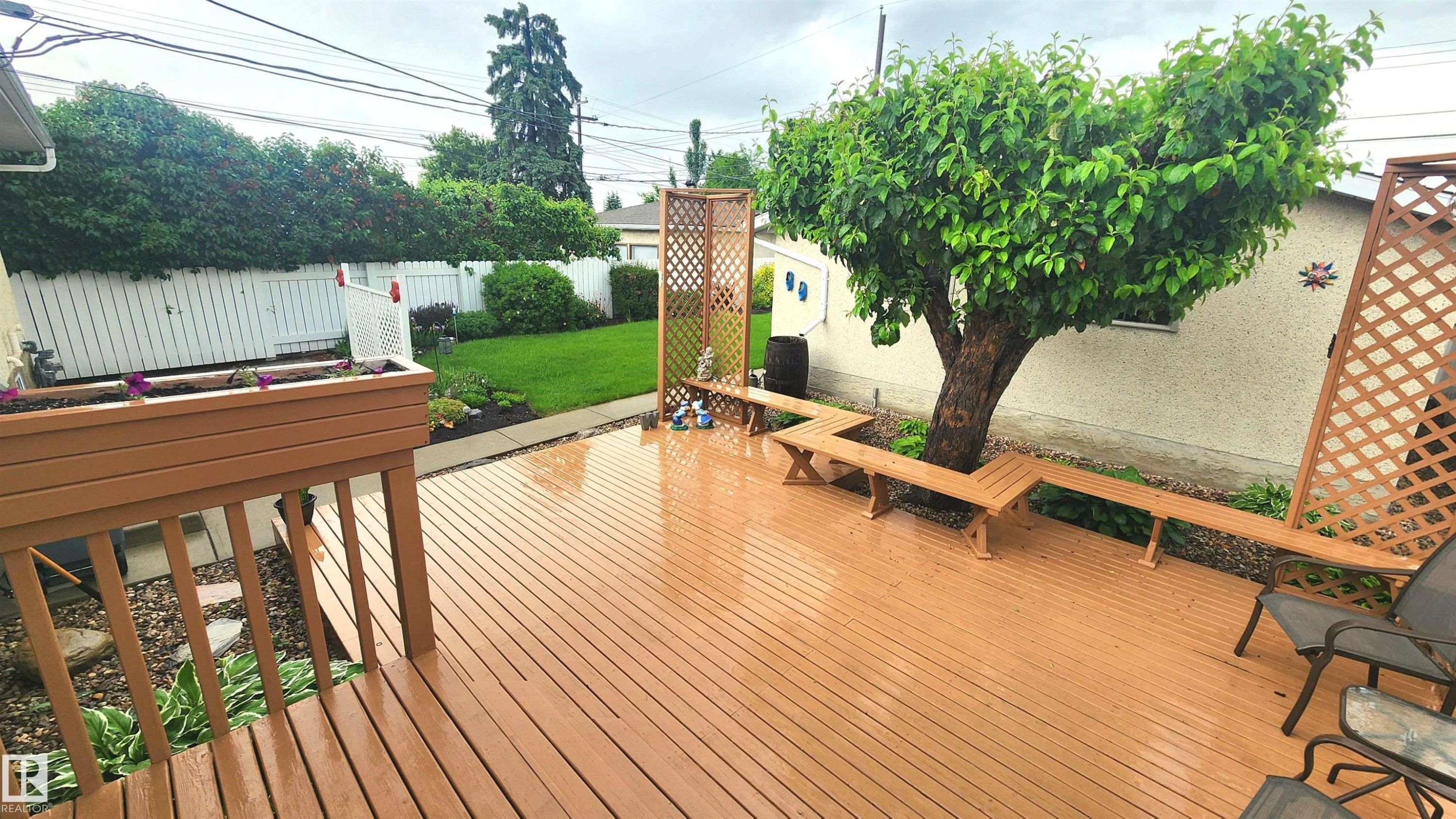 Expansive brown wood-finish deck featuring built-in perimeter seating and a central mature tree - 13307 Delwood Road, Edmonton, AB