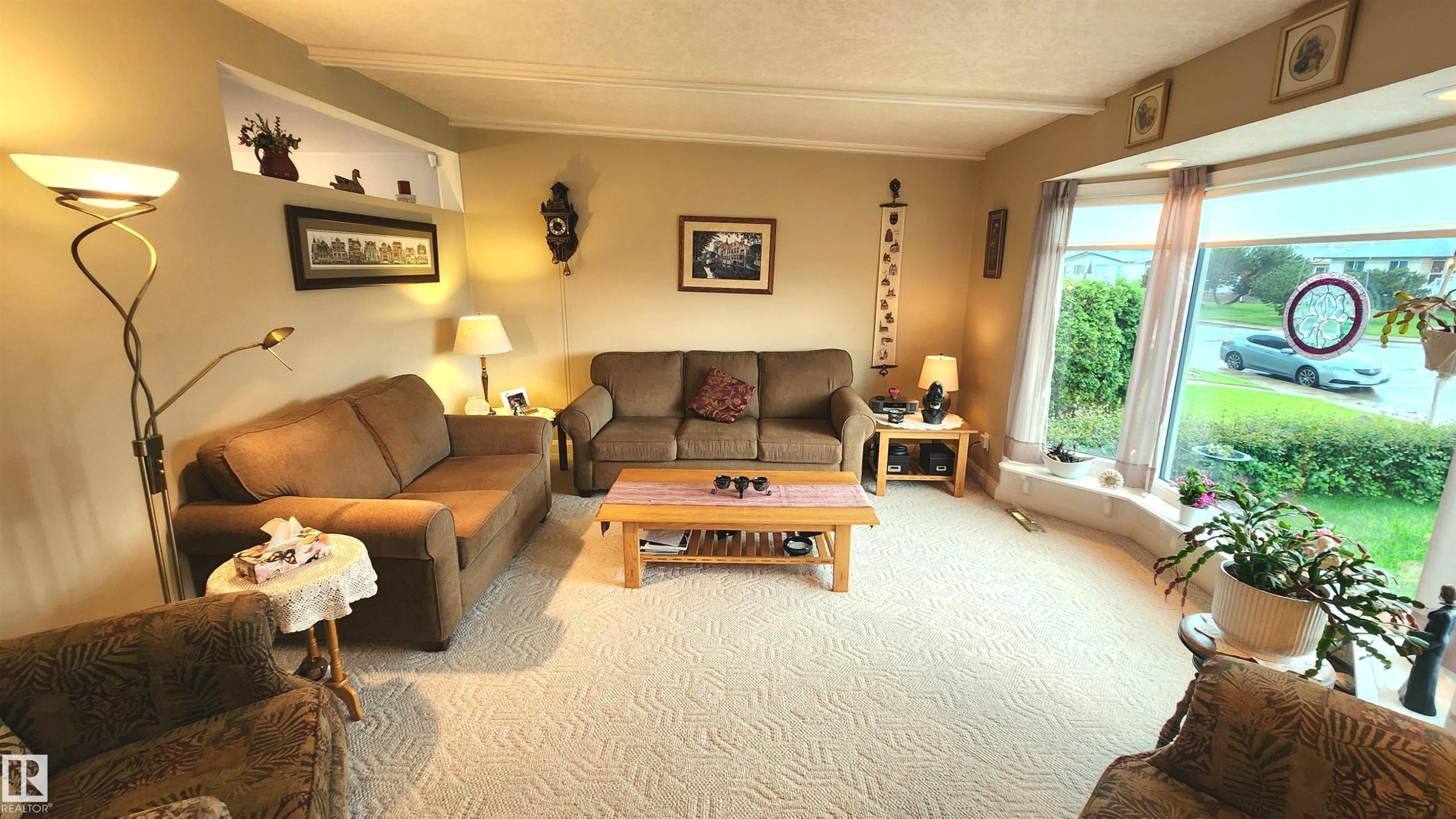 Living room featuring a large bay window, light-toned patterned carpeting, a built-in display nook, crown molding, and neutral wall tones - 13307 Delwood Road, Edmonton, AB