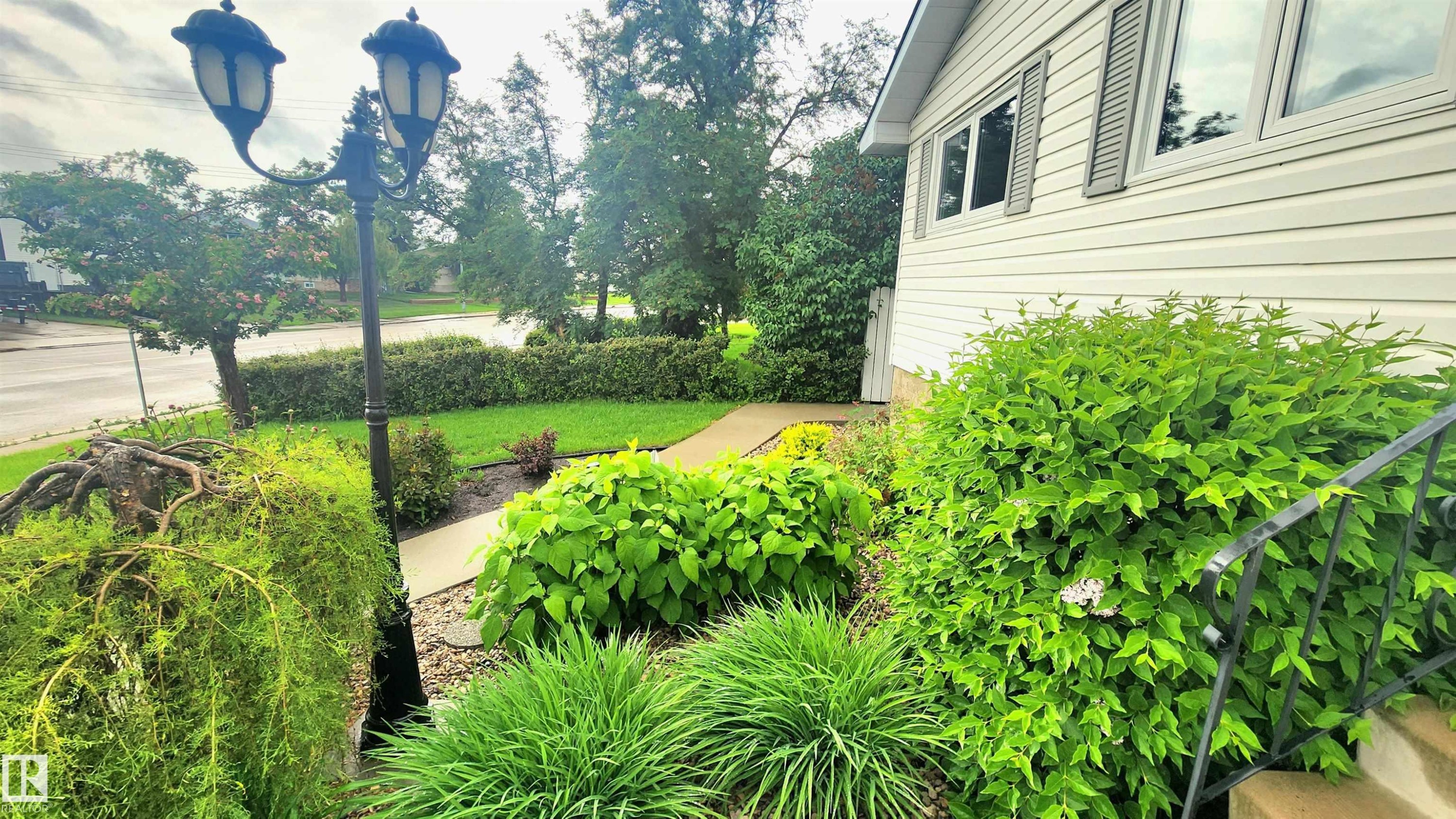 Manicured landscaping with diverse plantings, a concrete walkway, and a decorative street lamp - 13307 Delwood Road, Edmonton, AB