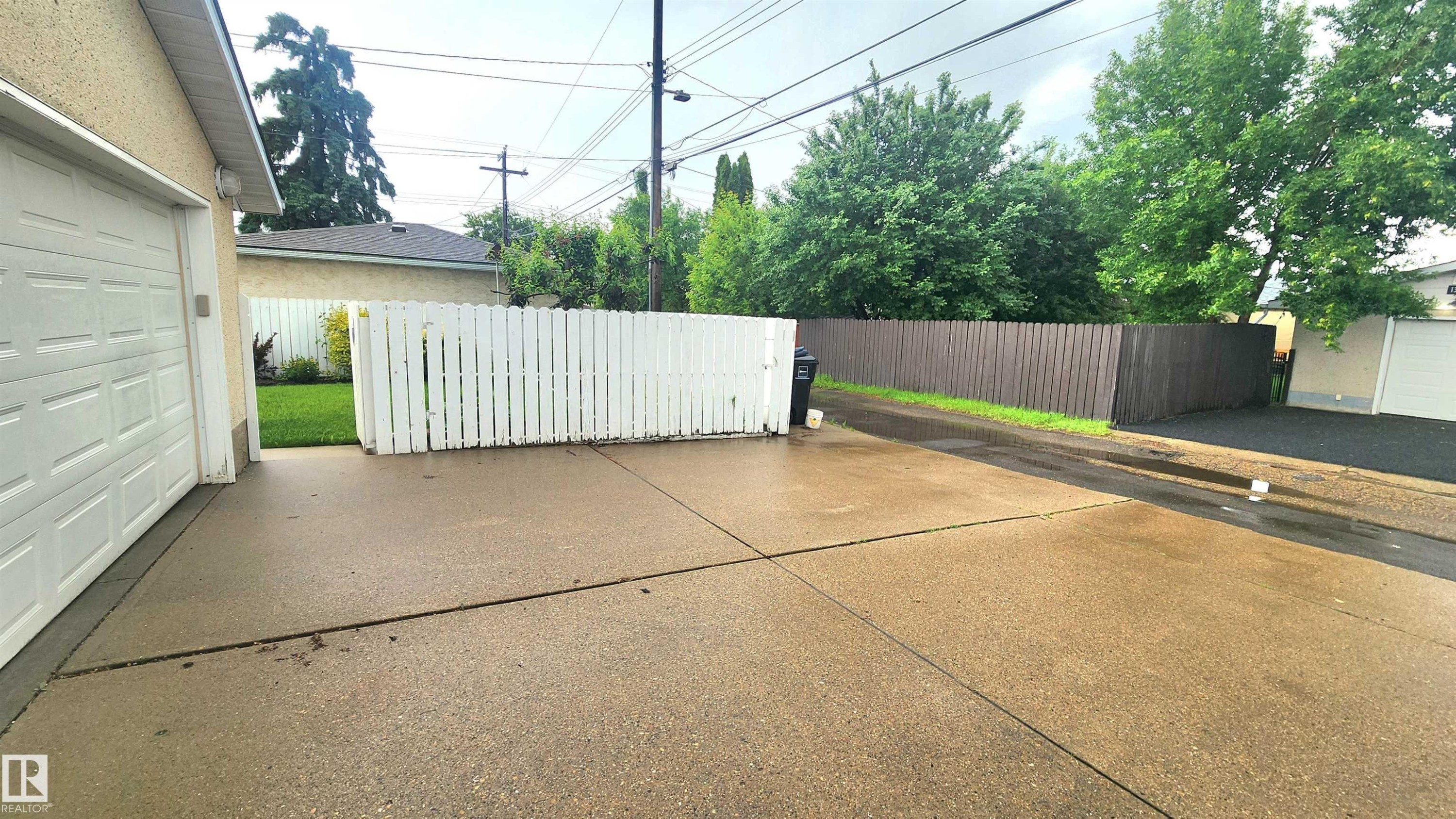 Expansive concrete driveway providing access to the attached garage, bordered by a white picket fence and a tall privacy fence - 13307 Delwood Road, Edmonton, AB