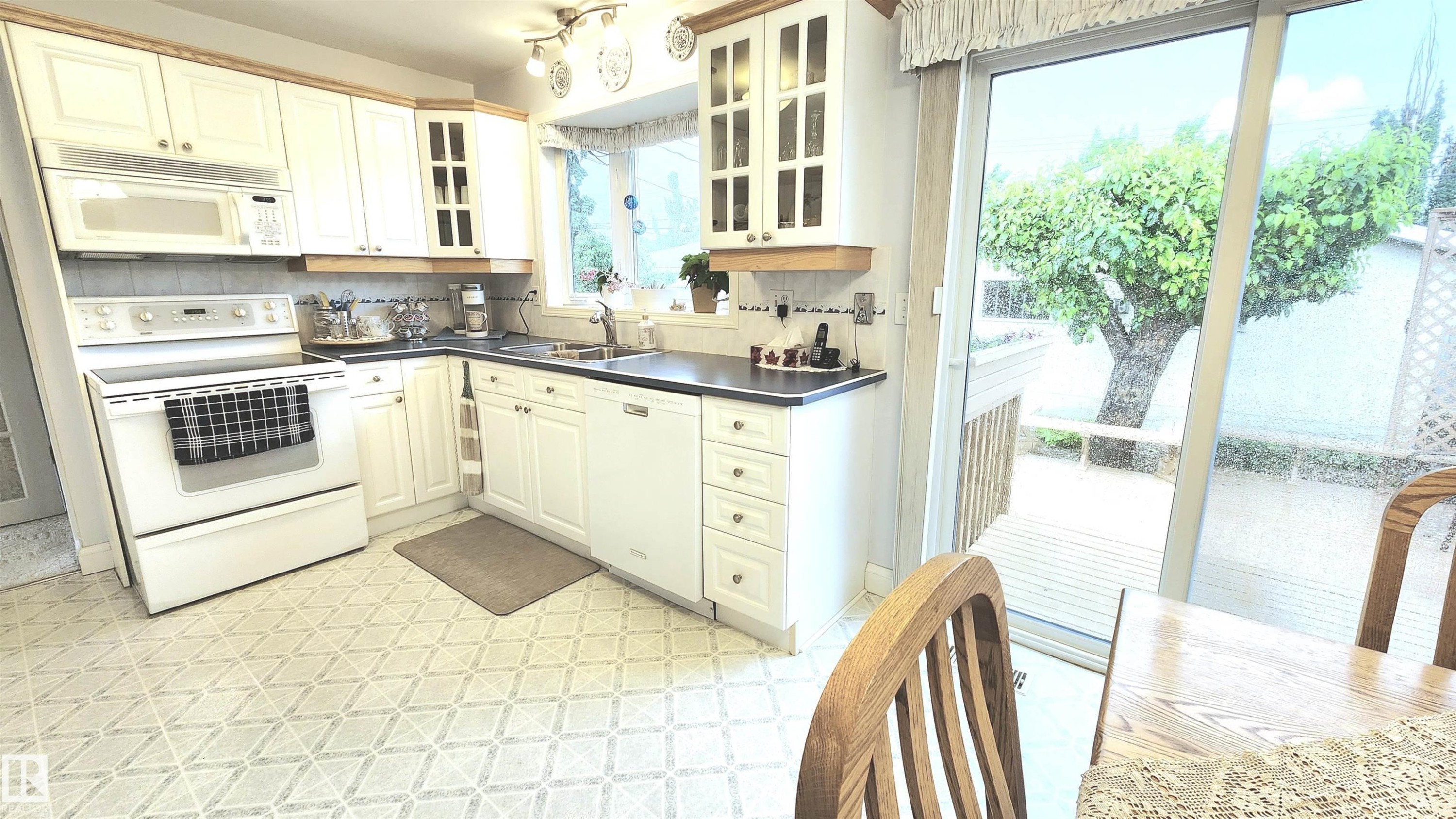White cabinetry kitchen featuring a built-in microwave, tile backsplash, and dark countertops, with patterned flooring - 13307 Delwood Road, Edmonton, AB