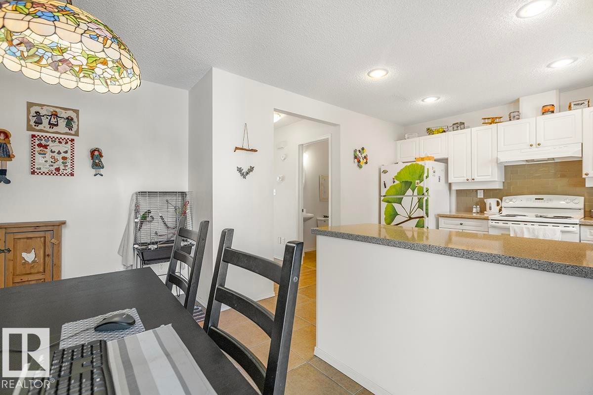 Bright kitchen featuring white cabinetry, a light-toned backsplash, and a breakfast bar with a speckled countertop - 44 9630 176 Street, Edmonton, AB