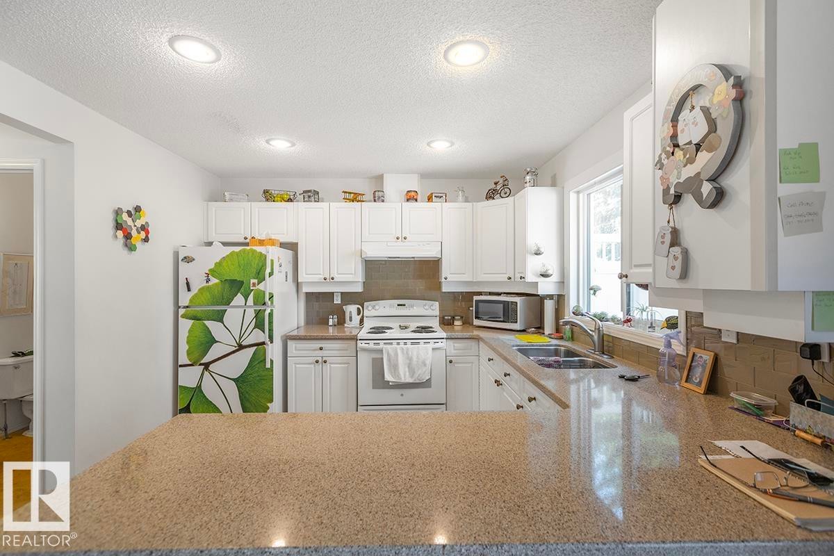 Kitchen featuring white cabinetry with brushed nickel hardware, a built-in electric range, and a double basin stainless steel sink - 44 9630 176 Street, Edmonton, AB