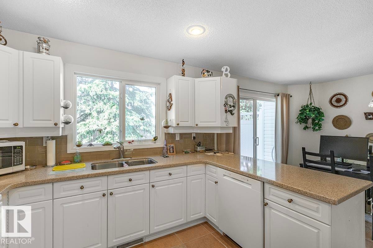 Kitchen featuring white cabinetry, a double basin stainless steel sink, light-colored countertops, and a full-size window - 44 9630 176 Street, Edmonton, AB