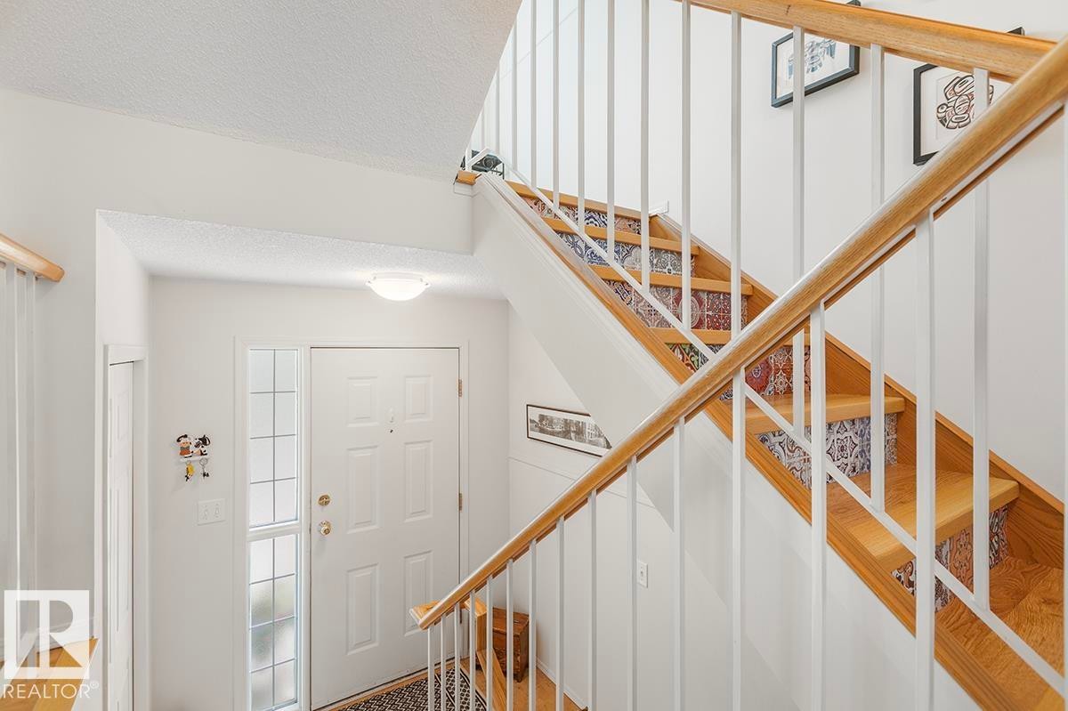 Entryway featuring a white paneled door with sidelight, overhead lighting, and a staircase with wood treads, patterned risers, and a wood handrail - 44 9630 176 Street, Edmonton, AB
