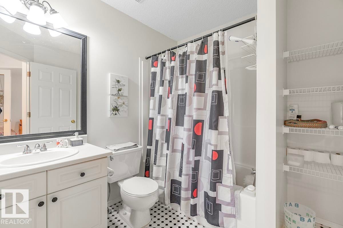 Bathroom featuring a white vanity with an undermount sink, a framed mirror, a toilet, a full bathtub with a shower, and wire shelving - 44 9630 176 Street, Edmonton, AB