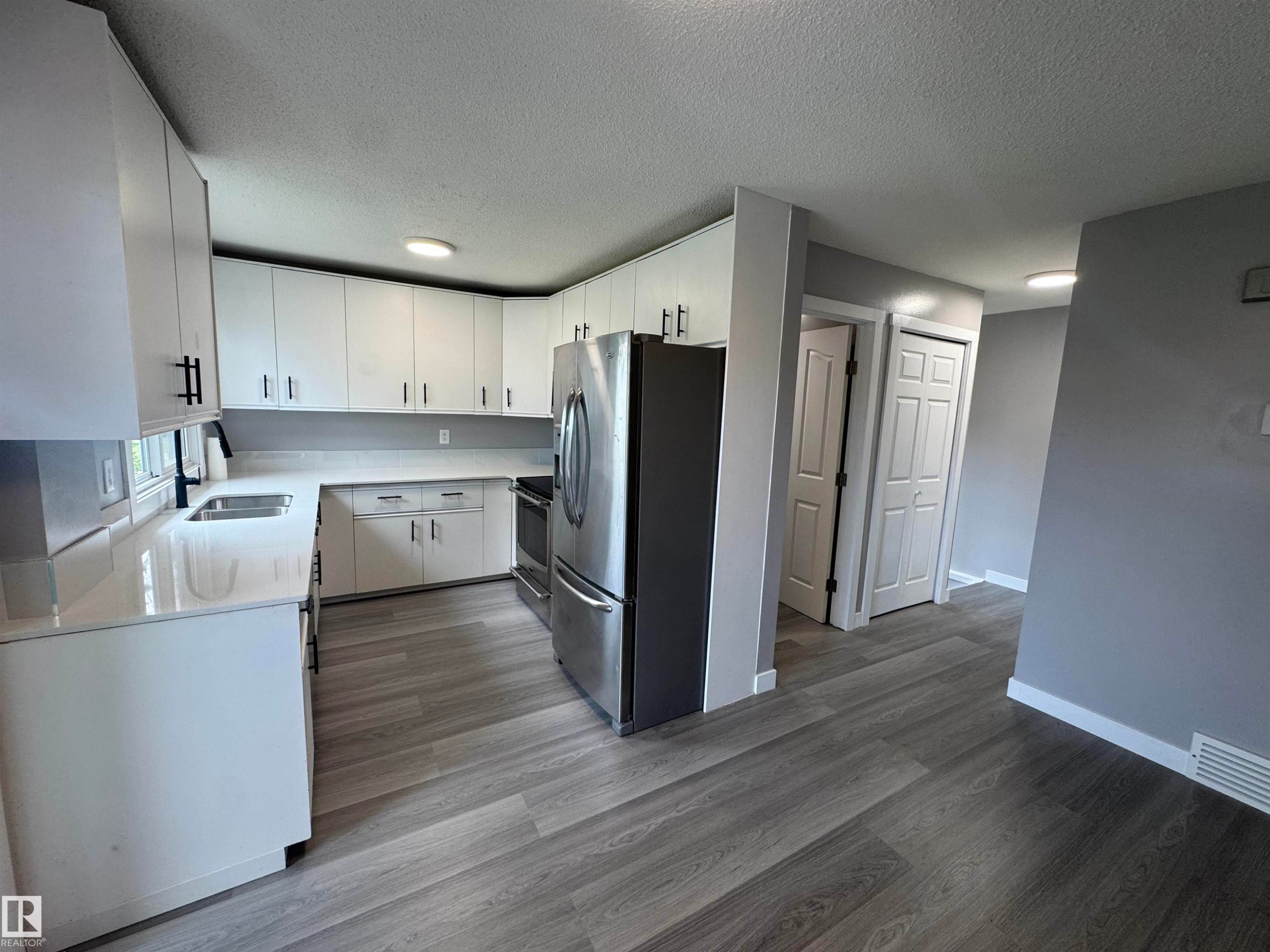 Modern kitchen featuring white cabinetry, light countertops, stainless steel appliances, and wood-finish flooring - 6441 180 Street, Edmonton, AB