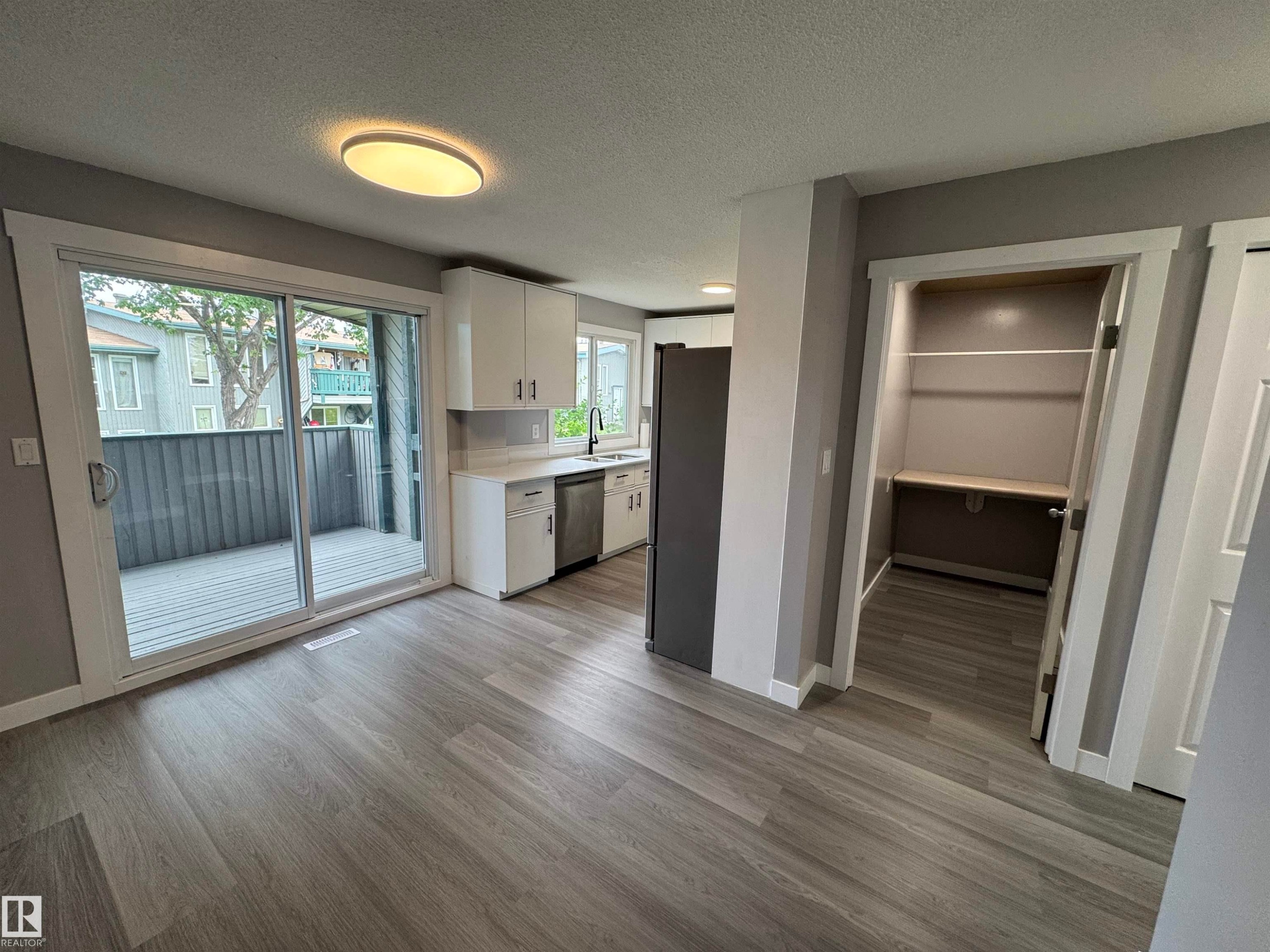 Modern kitchen and dining area featuring wood-finish flooring, white cabinetry, integrated stainless steel appliances, and a sliding glass door opening to a private deck - 6441 180 Street, Edmonton, AB