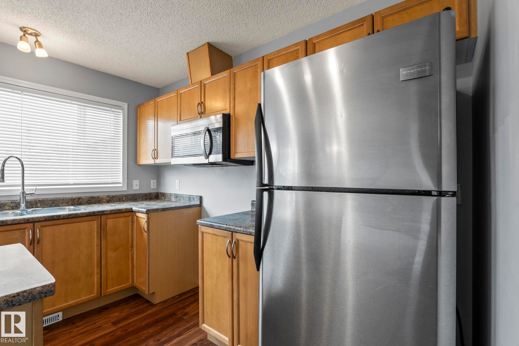 Kitchen featuring wood-finish cabinetry, speckled countertops, stainless steel appliances, and wood-finish flooring - 7118 19A, Edmonton, AB - Indoor Photo Showing Kitchen With Double Sink