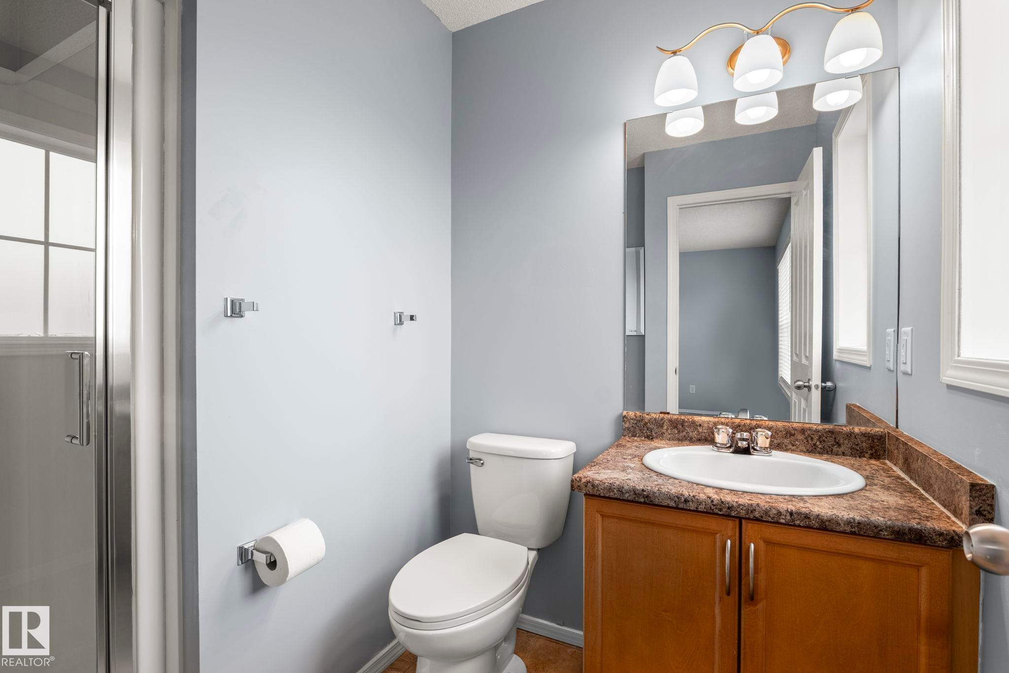 Bathroom featuring a white toilet, wood-finish vanity with a built-in sink, and a light-toned countertop - 7118 19A, Edmonton, AB - Indoor Photo Showing Bathroom