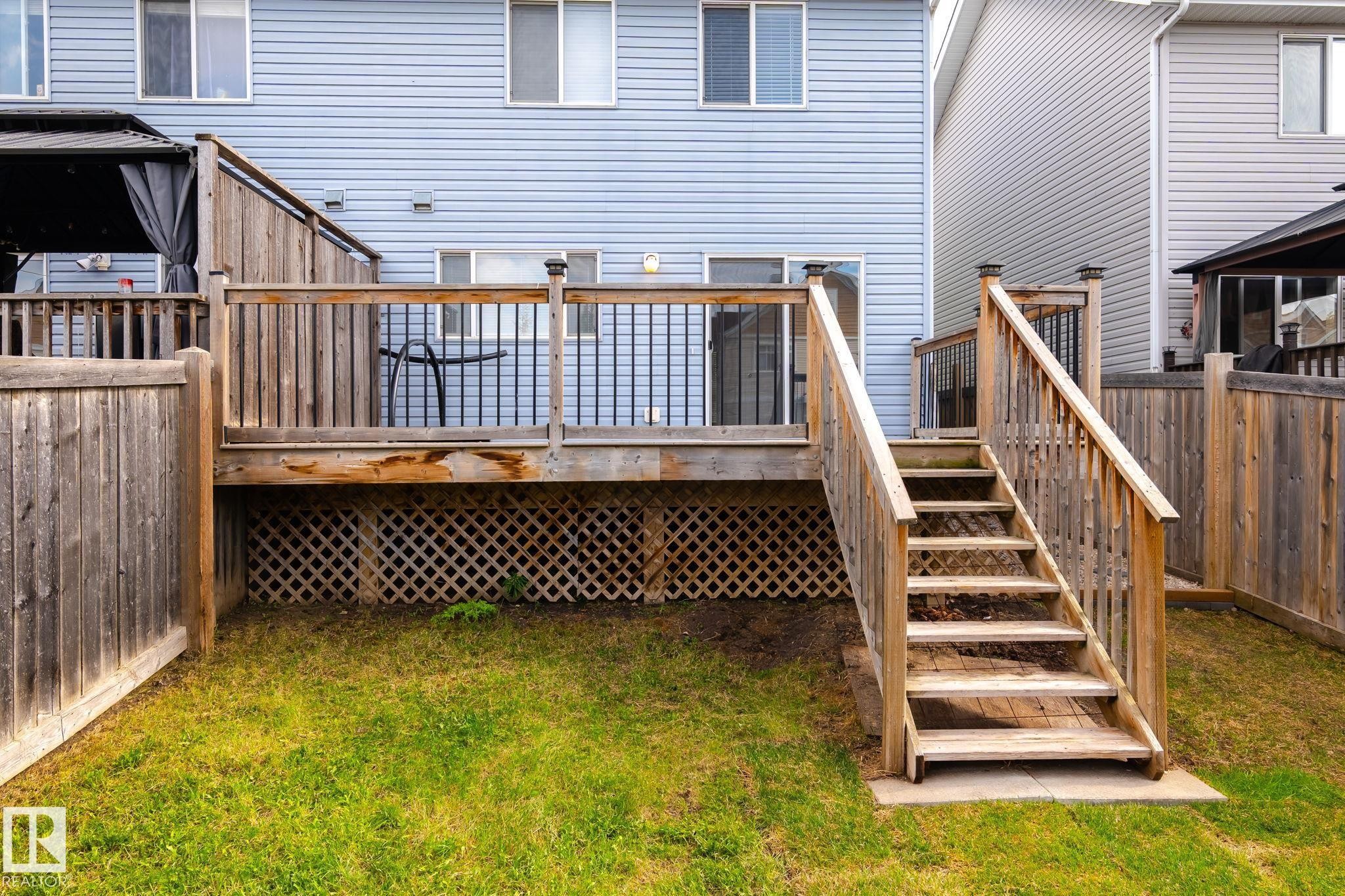 Wood-finish deck with stairs and lattice skirting, featuring a privacy fence and a grassy yard - 7118 19A, Edmonton, AB - Outdoor With Deck Patio Veranda With Exterior