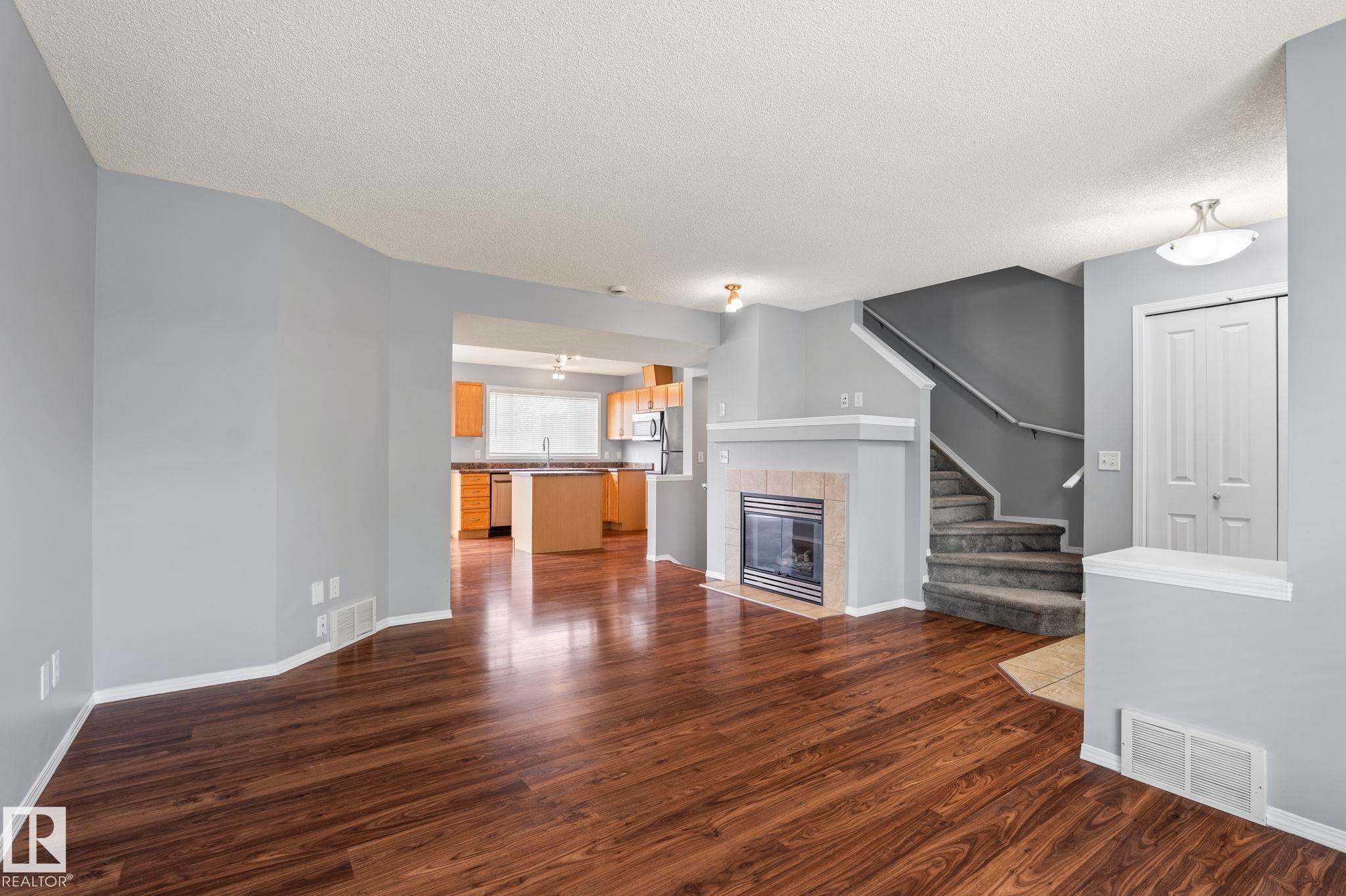 Open concept living area featuring dark wood-finish flooring, a gas fireplace with a light-toned tile surround, and a white mantel - 7118 19A, Edmonton, AB - Indoor Photo Showing Other Room With Fireplace