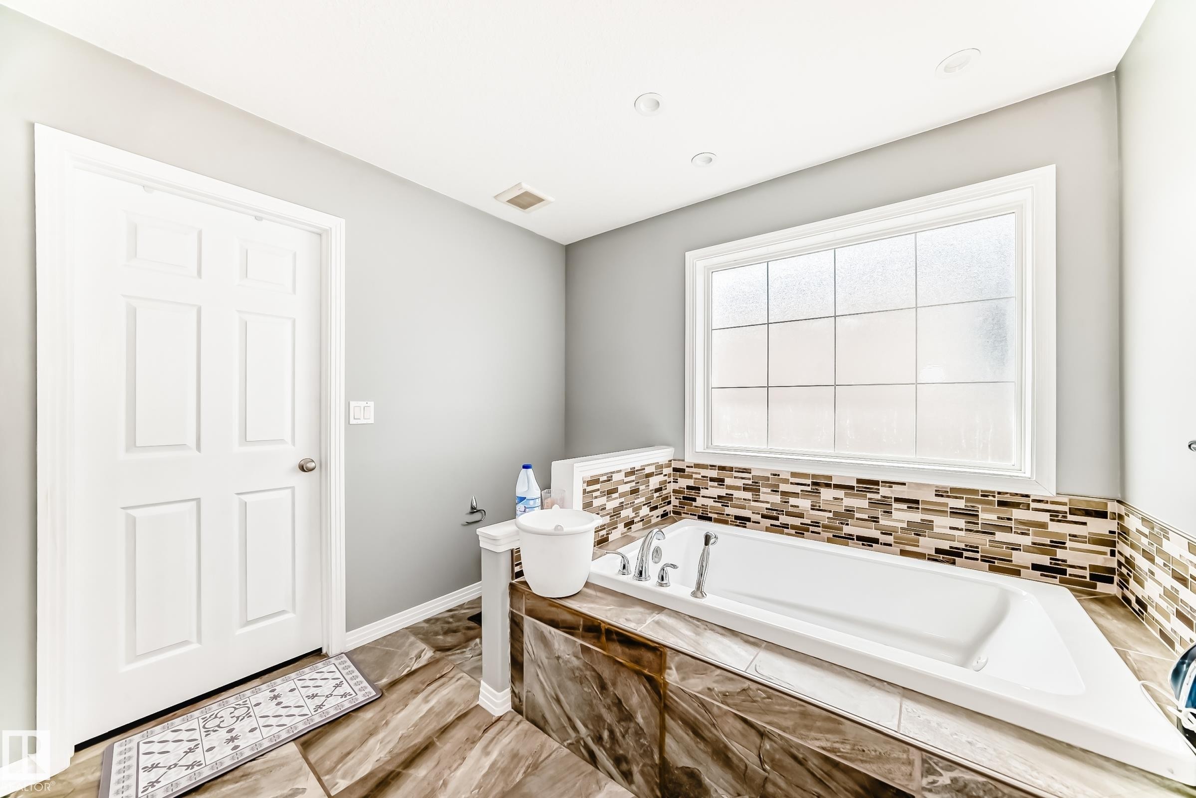 Built-in soaking tub featuring a decorative mosaic tile surround and a large privacy window - 16720 61 Street Nw, Edmonton, AB - Indoor Photo Showing Bathroom