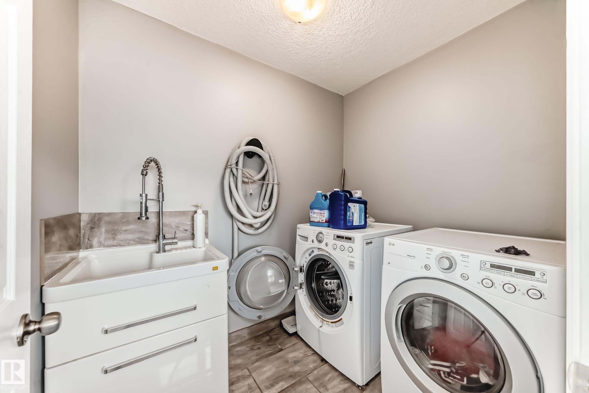 Dedicated utility space featuring a laundry sink with a gooseneck faucet, light gray wall paint, wood-finish flooring, and a ceiling-mounted light fixture - 16720 61 Street Nw, Edmonton, AB - Indoor Photo Showing Laundry Room