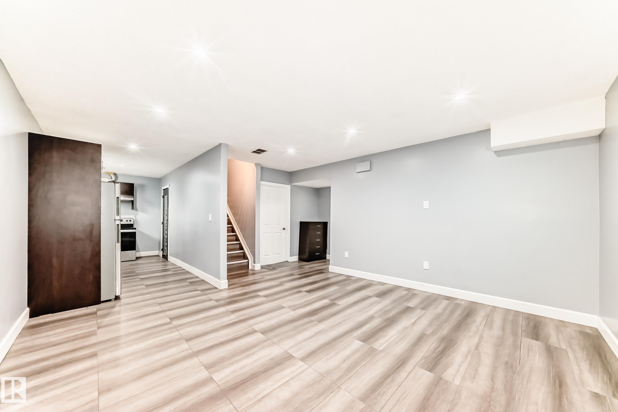 Open-concept living space featuring wood-finish flooring, recessed lighting, a neutral gray color palette, white baseboards, and a visible staircase with wood treads - 16720 61 Street Nw, Edmonton, AB - Indoor