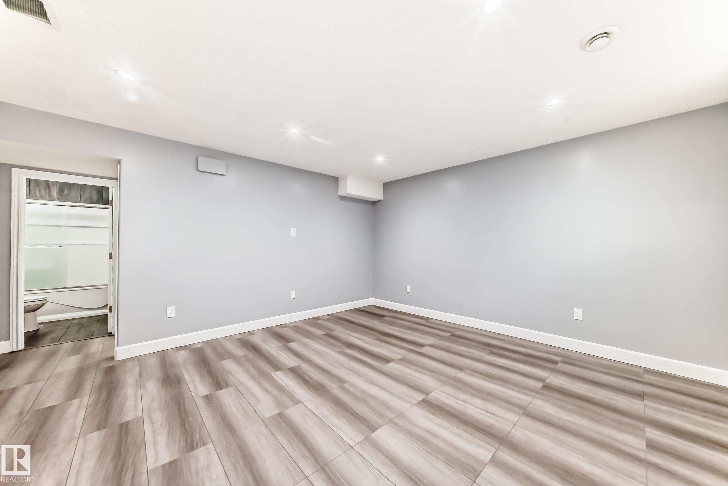 Spacious room featuring wood-finish flooring, light gray walls, recessed lighting, and white baseboards - 16720 61 Street Nw, Edmonton, AB - Indoor