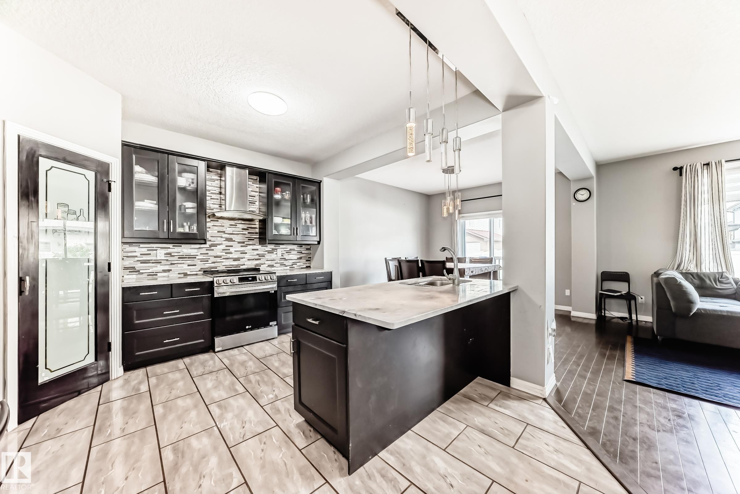 Kitchen featuring dark cabinetry, stainless steel appliances, a patterned tile backsplash, and a central island with a sink and pendant lighting - 16720 61 Street Nw, Edmonton, AB - Indoor
