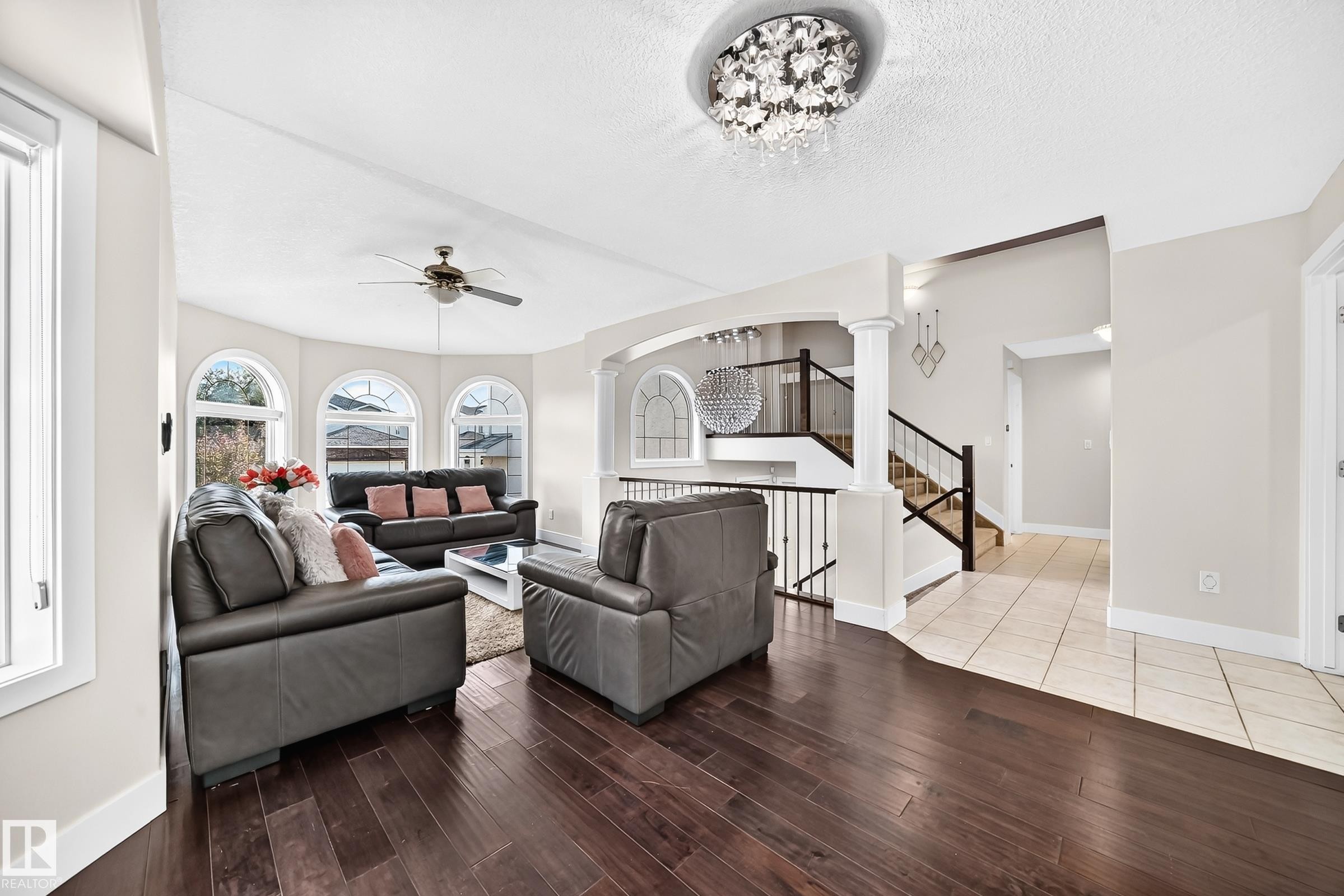 Spacious living area featuring dark wood-finish flooring, a contemporary chandelier, and a ceiling fan - 16124 76 Street, Edmonton, AB