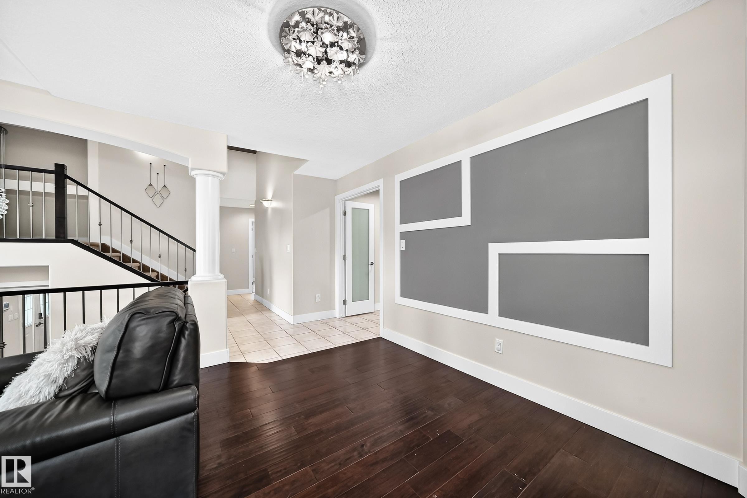 Interior space featuring dark wood-finish flooring, a decorative wall panel with a gray inset, a crystal flush mount ceiling light, and a staircase with dark railings - 16124 76 Street, Edmonton, AB