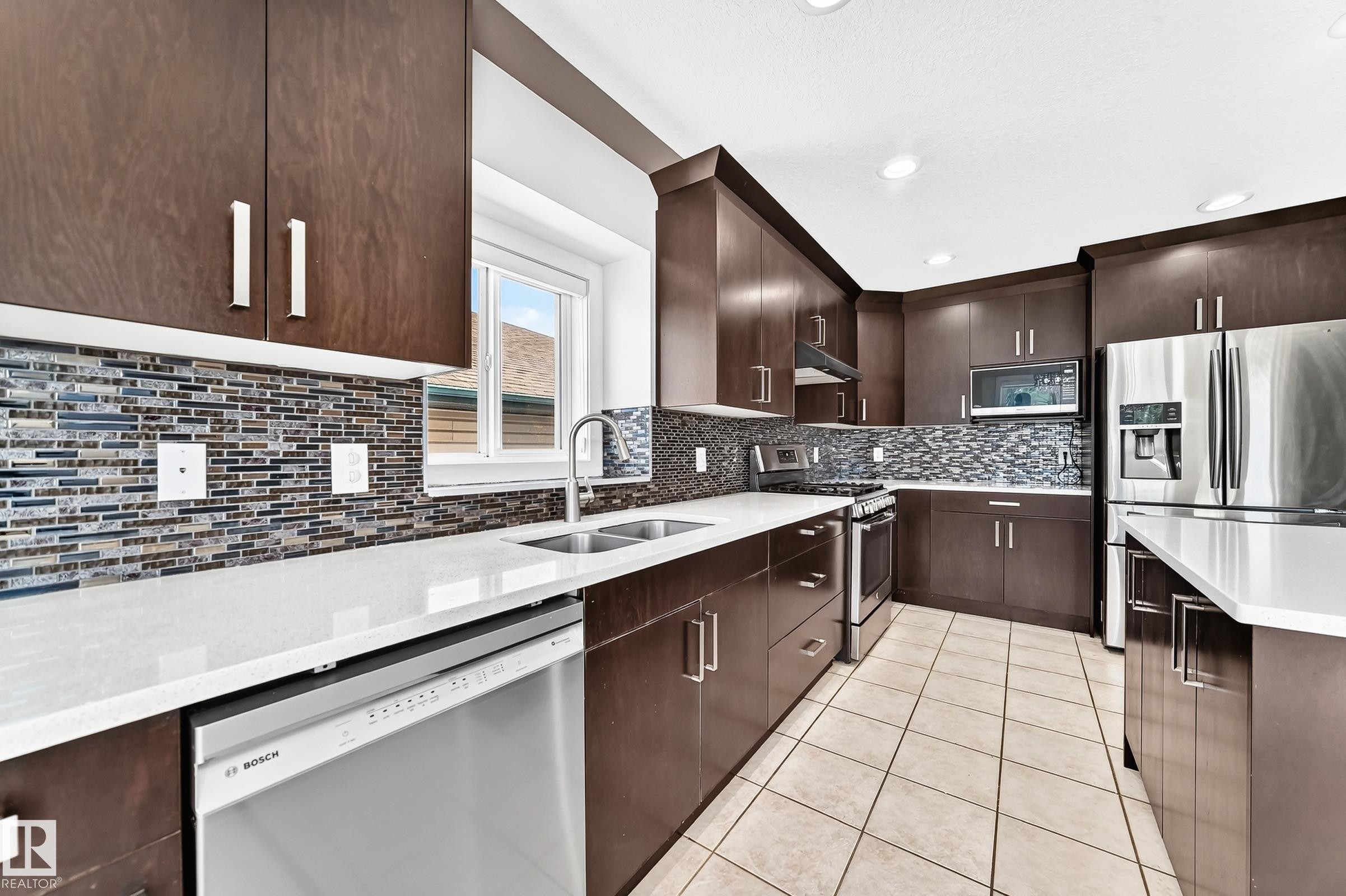 Modern kitchen featuring dark wood-finish cabinetry, stainless steel appliances, and light-toned countertops - 16124 76 Street, Edmonton, AB
