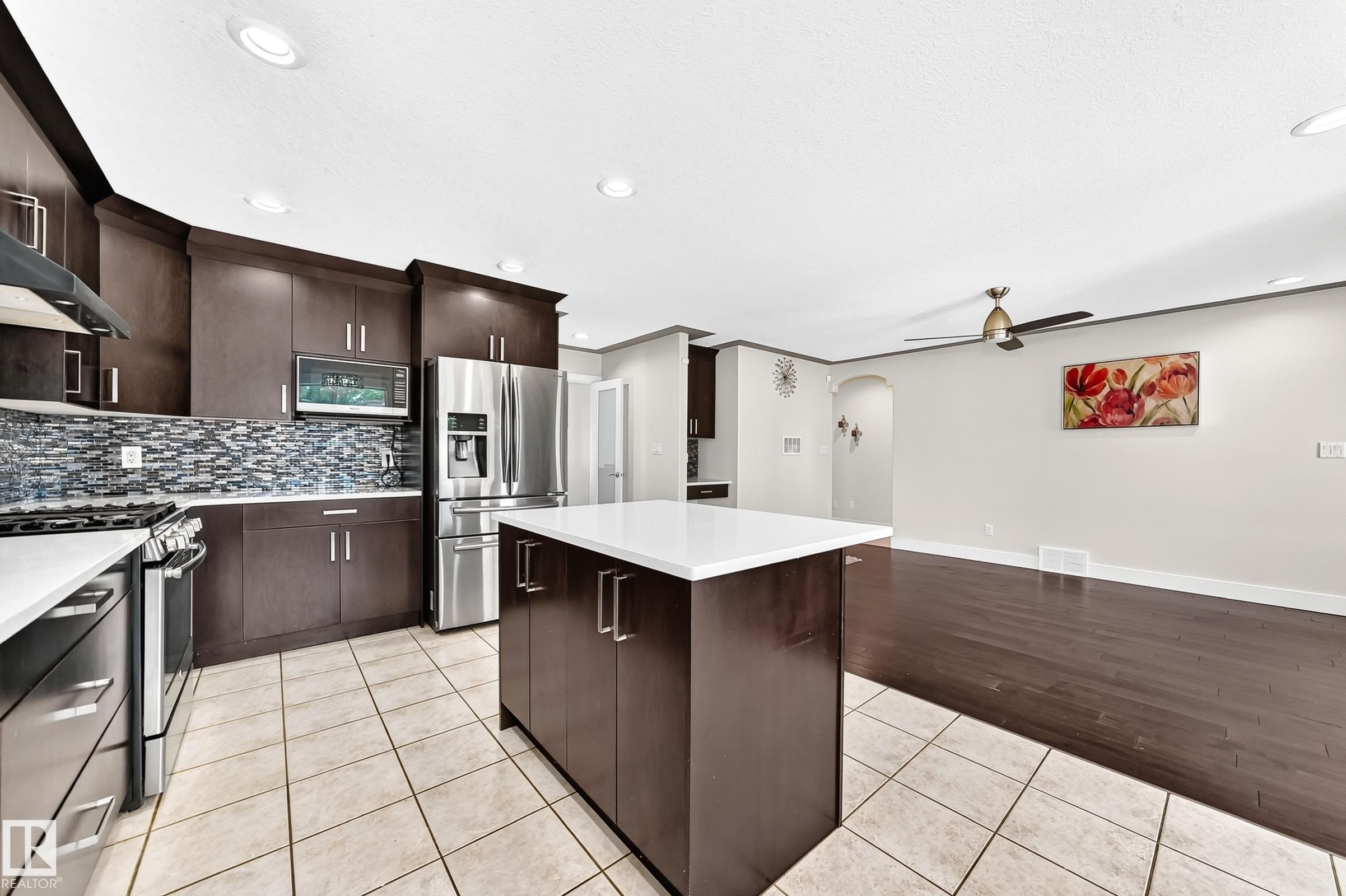 Modern kitchen featuring espresso cabinetry, stainless steel appliances, a white quartz island, and a mosaic tile backsplash - 16124 76 Street, Edmonton, AB