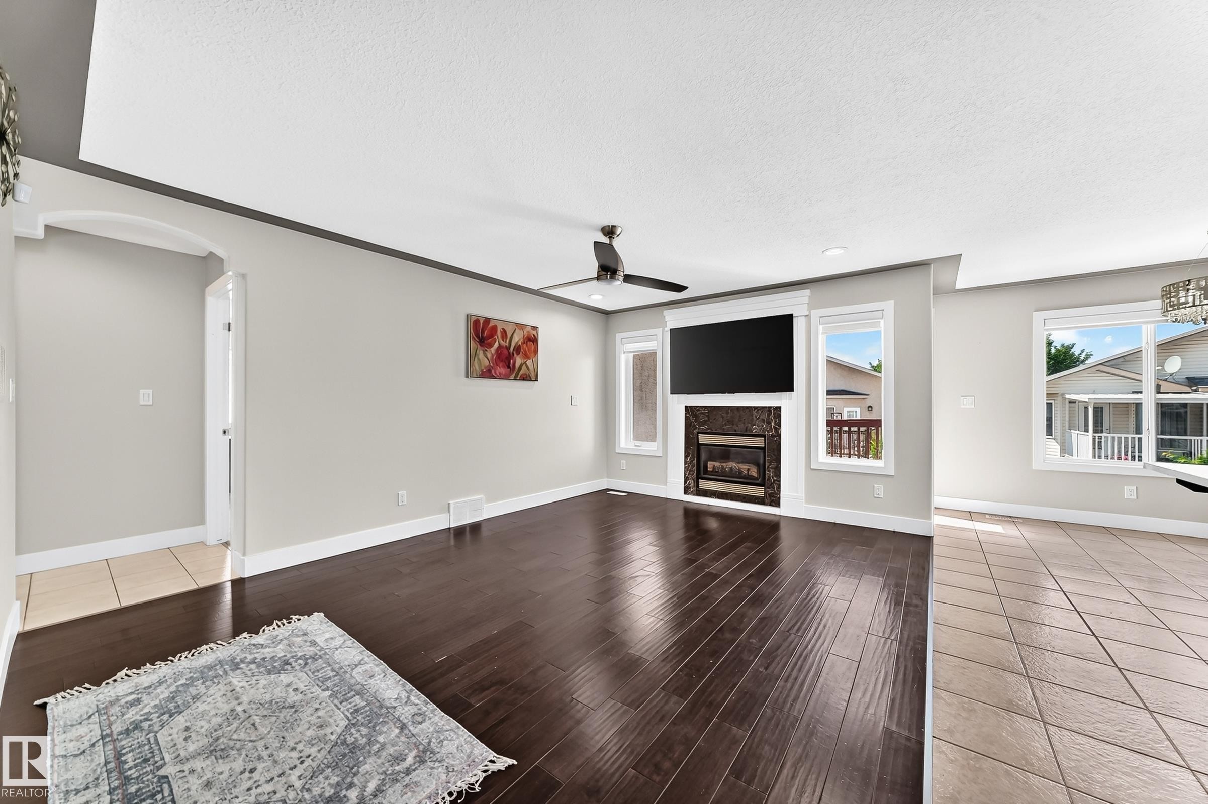 Spacious living area featuring wood-finish flooring, a ceiling fan, and a built-in fireplace with a stone surround - 16124 76 Street, Edmonton, AB