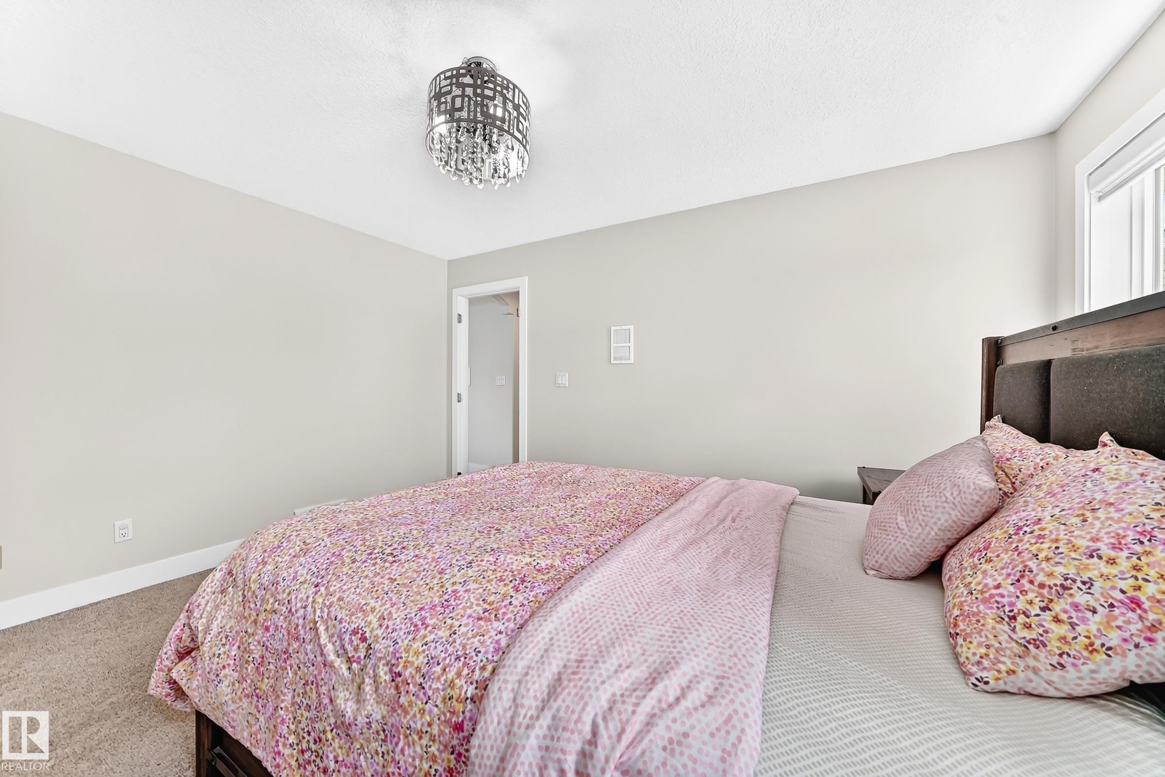 Bedroom featuring a contemporary chandelier, neutral wall paint, white trim, and a window providing natural light - 16124 76 Street, Edmonton, AB