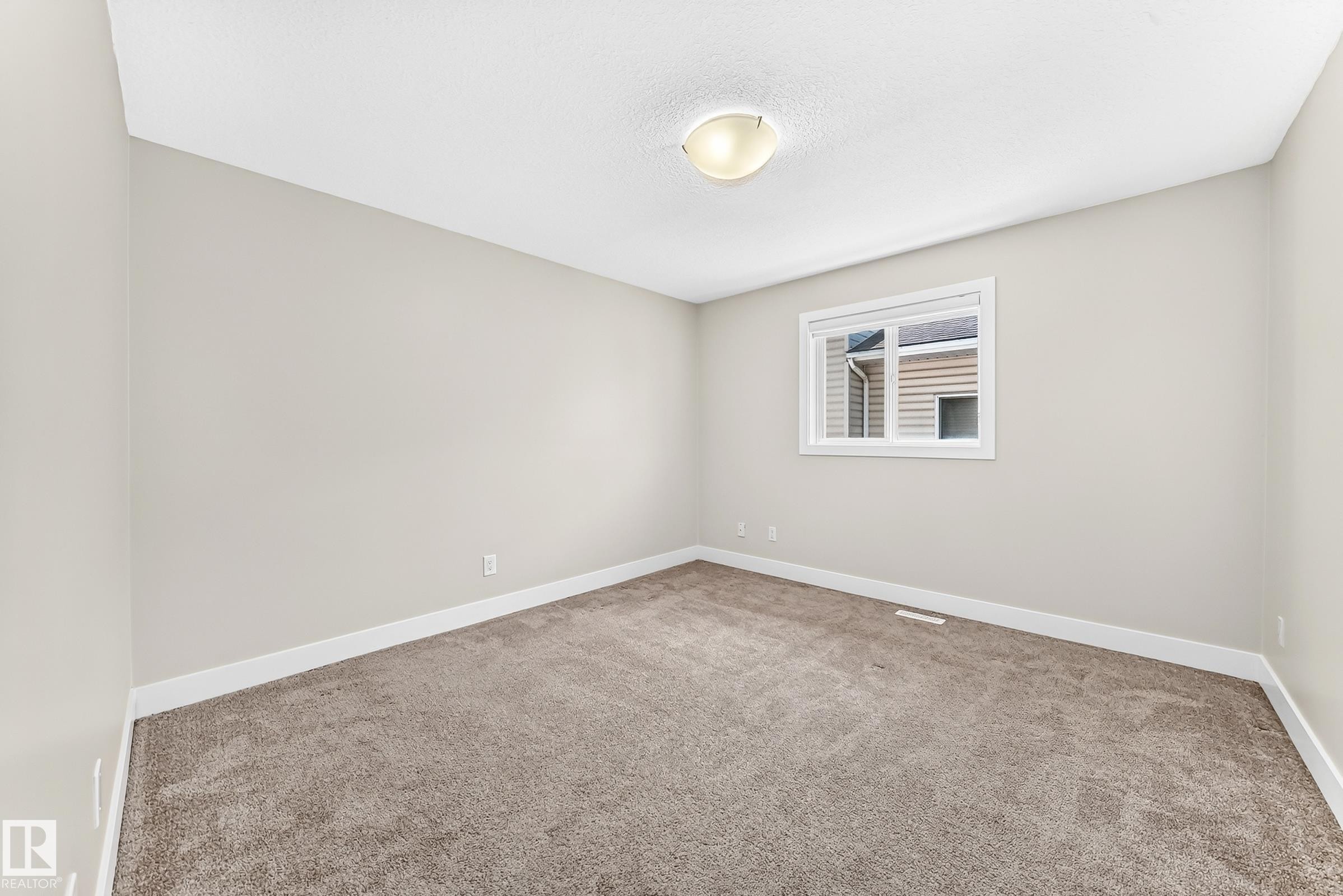 Carpeted interior room featuring light gray wall paint, white trim, a single window, and a flush-mount ceiling light fixture - 16124 76 Street, Edmonton, AB