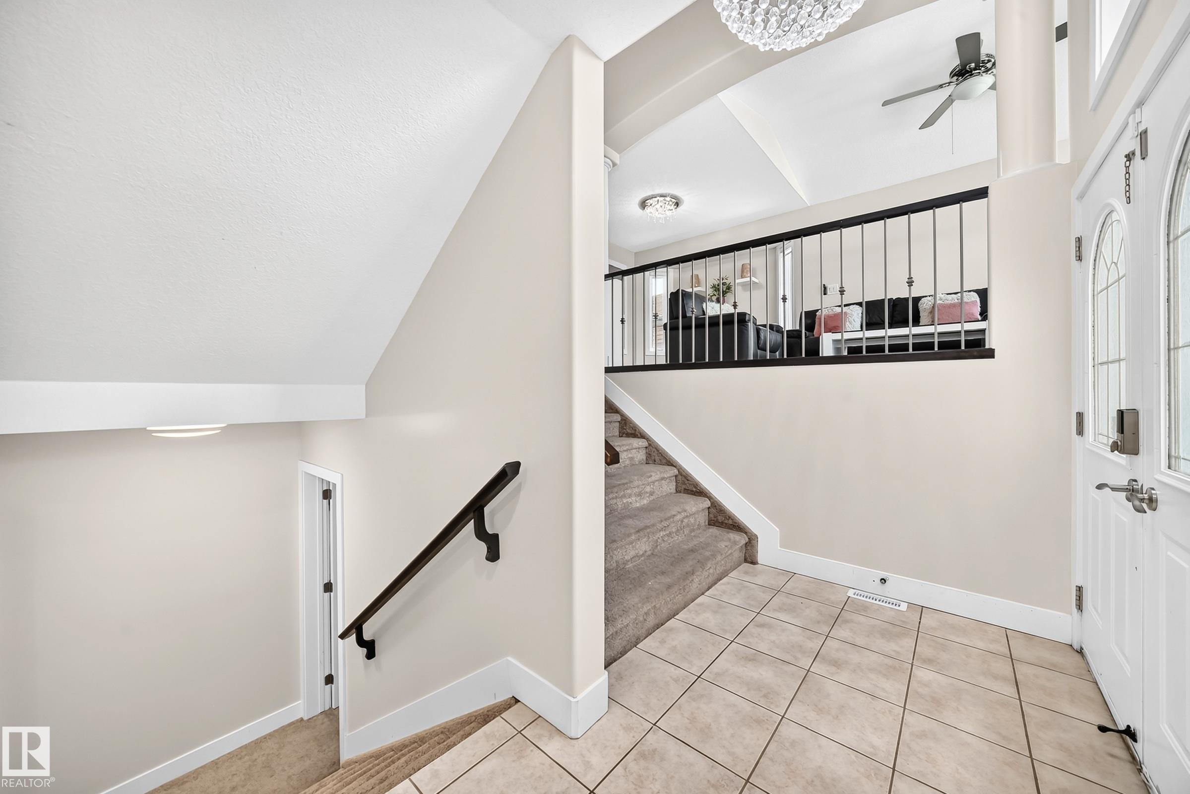 Foyer entry featuring ceramic tile flooring, a white paneled front door with decorative glass inserts, and a black wrought iron staircase railing - 16124 76 Street, Edmonton, AB