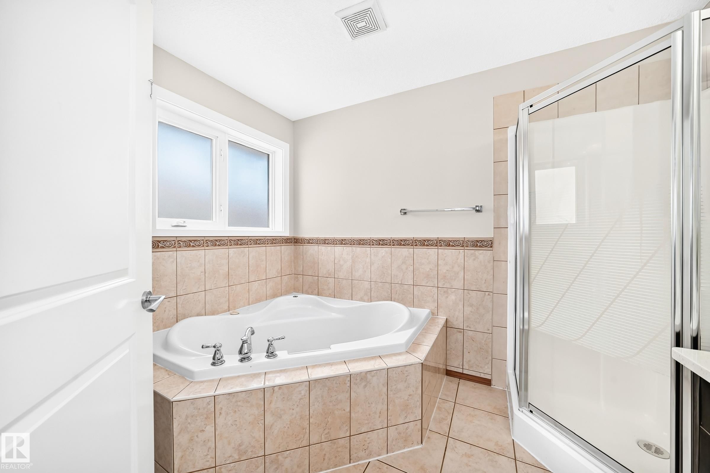 Bathroom featuring a corner soaking tub with deck-mounted fixtures, a glass-enclosed shower, and tiled surround - 16124 76 Street, Edmonton, AB