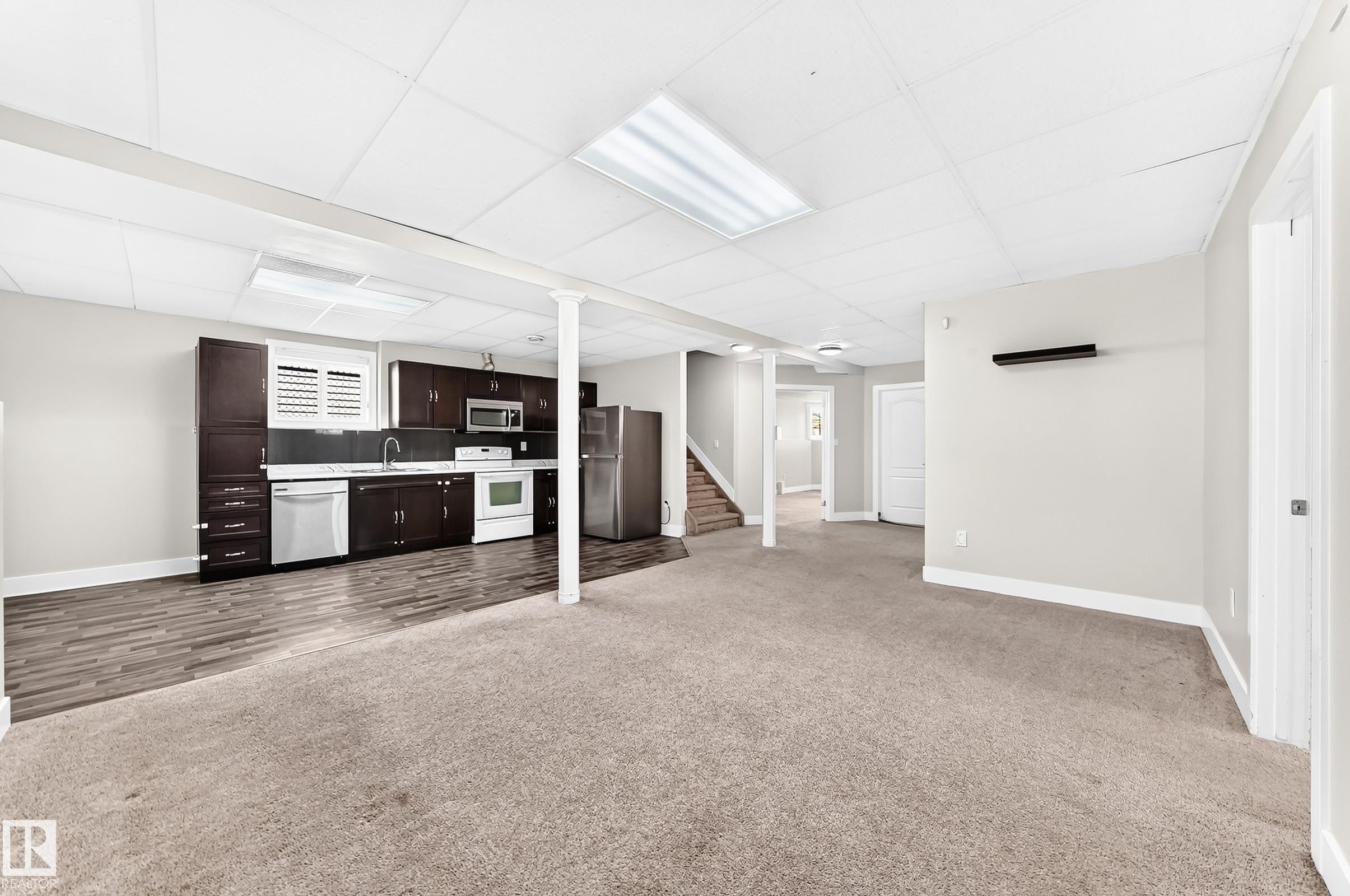 Open concept living area featuring a full kitchen with dark wood-finish cabinetry, stainless steel appliances, and a wood-finish flooring - 16124 76 Street, Edmonton, AB