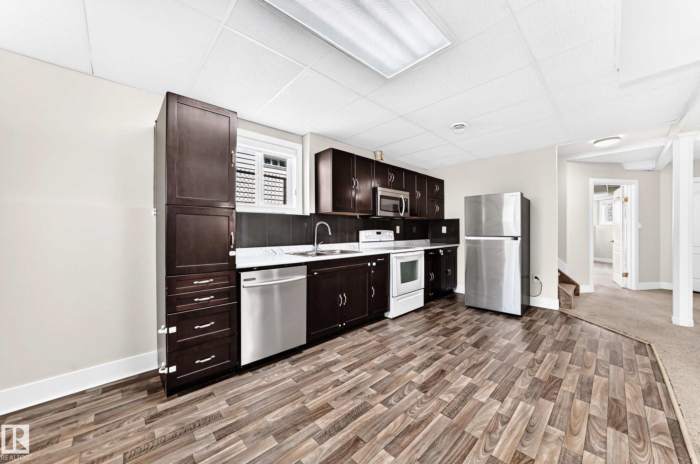 Kitchen area featuring dark wood cabinetry, stainless steel appliances, a white countertop, and wood-finish flooring - 16124 76 Street, Edmonton, AB