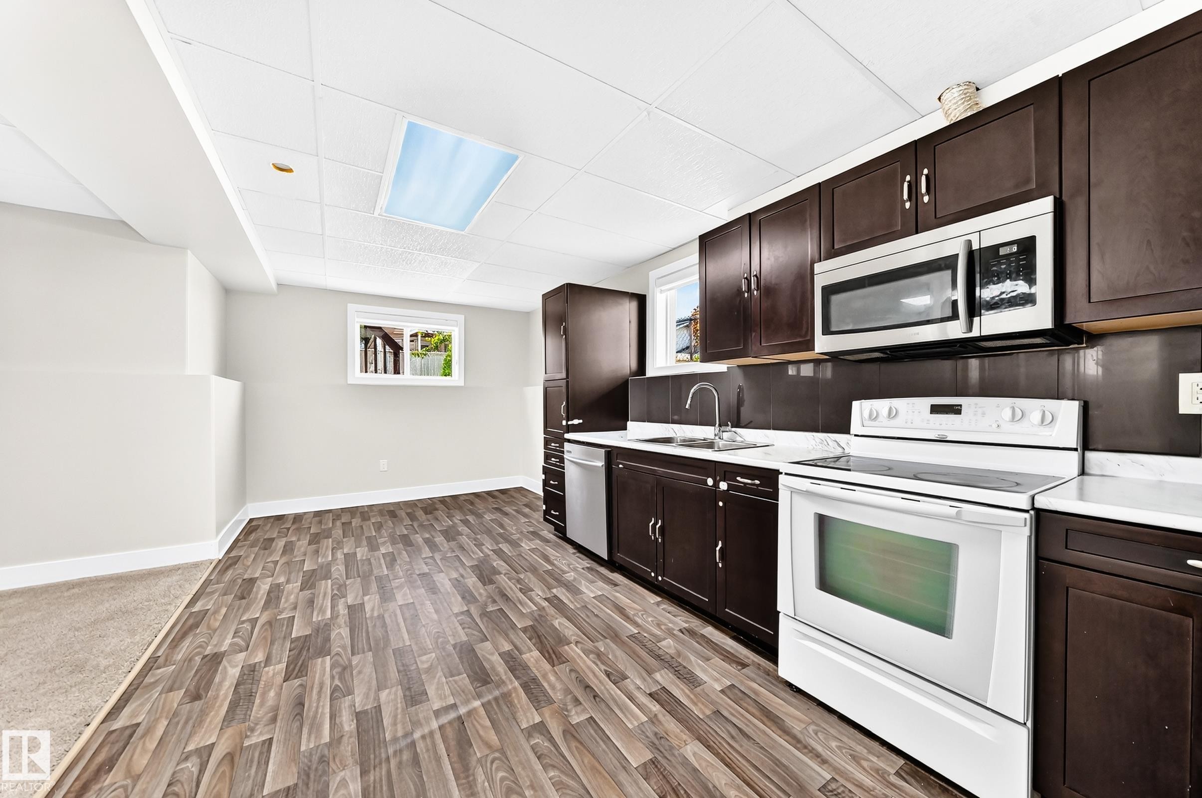 Kitchen featuring dark wood-finish cabinetry, white countertops, and a full suite of appliances including a stainless steel microwave and dishwasher - 16124 76 Street, Edmonton, AB