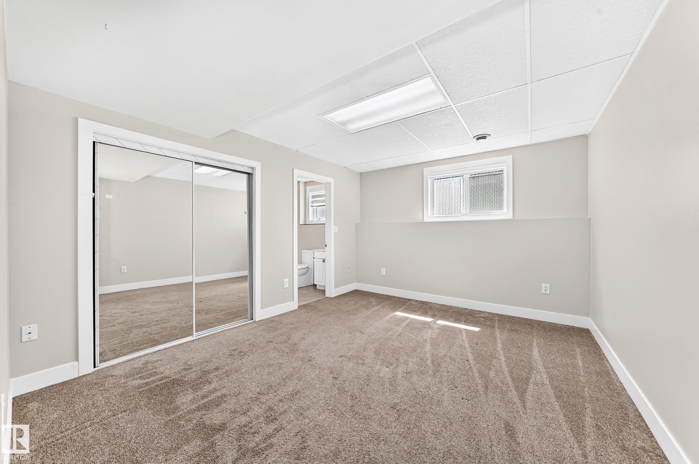 Carpeted room featuring mirrored sliding closet doors, neutral wall paint, white trim, and a drop ceiling with integrated lighting - 16124 76 Street, Edmonton, AB