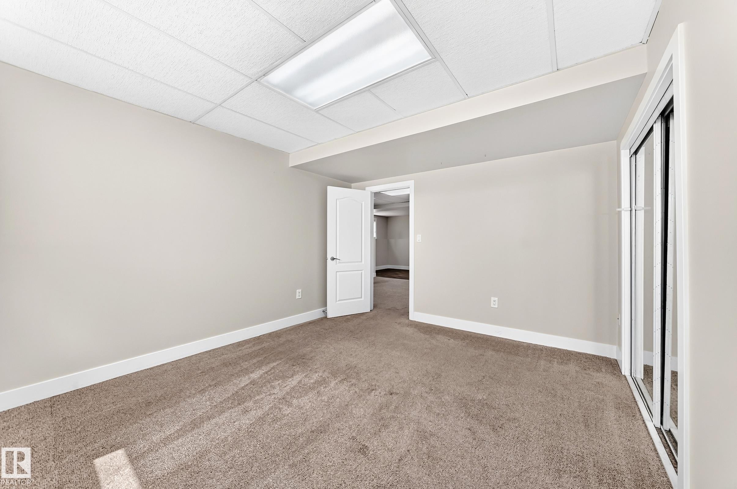 Spacious room featuring neutral paint, tan carpeting, white baseboards, and a drop ceiling with recessed lighting - 16124 76 Street, Edmonton, AB