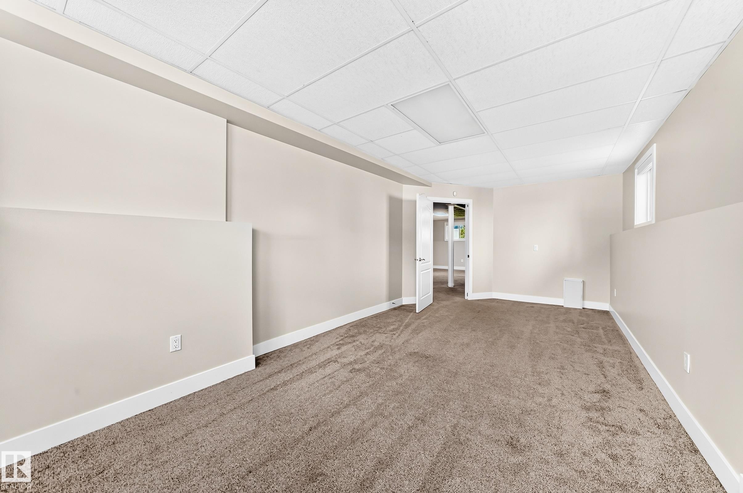 Spacious room featuring new carpeting, neutral wall paint, white trim, a drop ceiling with integrated lighting, and an egress window - 16124 76 Street, Edmonton, AB