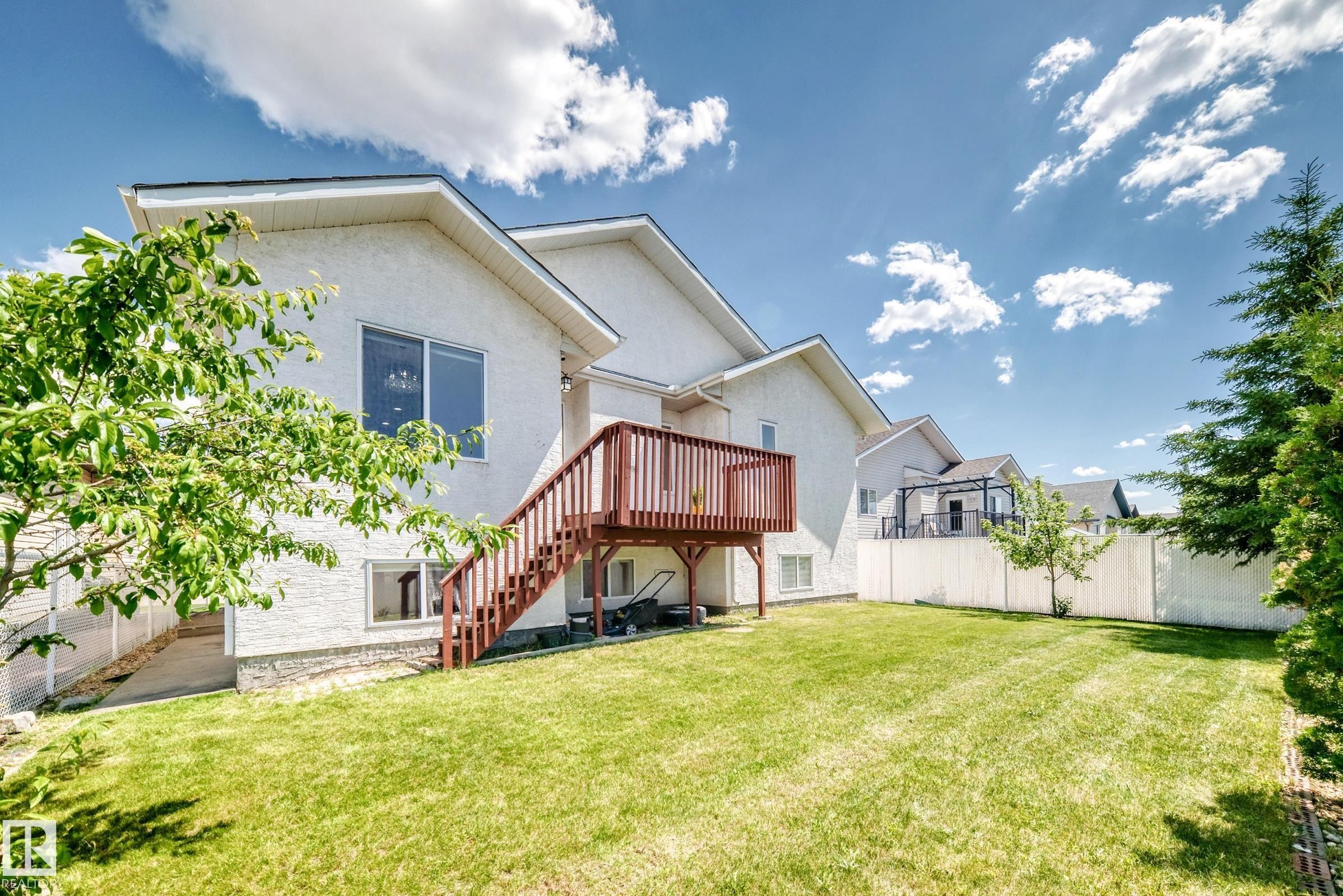 Expansive backyard featuring a manicured lawn, a two-story residence with white stucco siding, and a wood deck with stairs - 16124 76 Street, Edmonton, AB