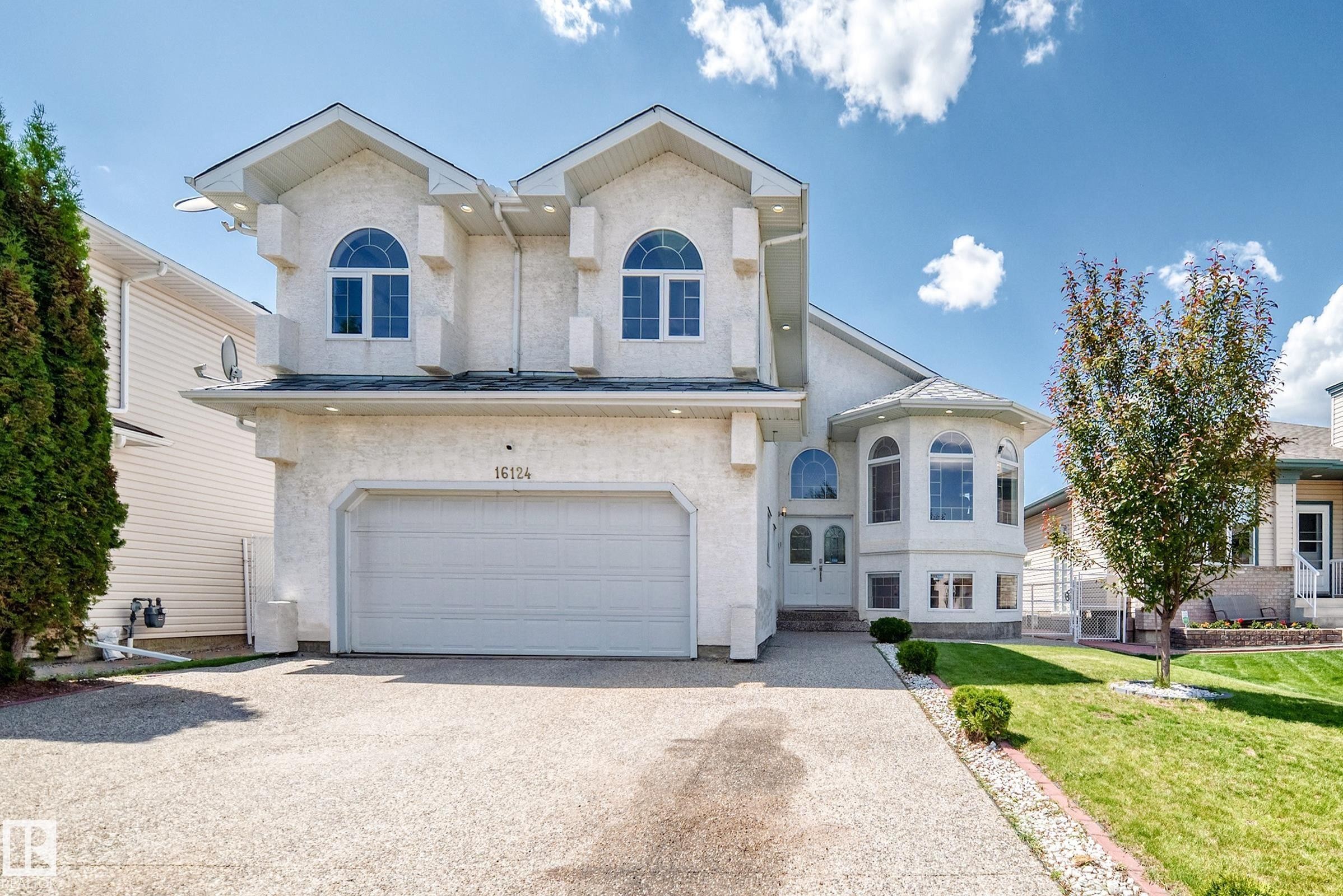 Stucco-clad exterior with prominent arched windows, a two-car garage, and a curved bay window feature - 16124 76 Street, Edmonton, AB