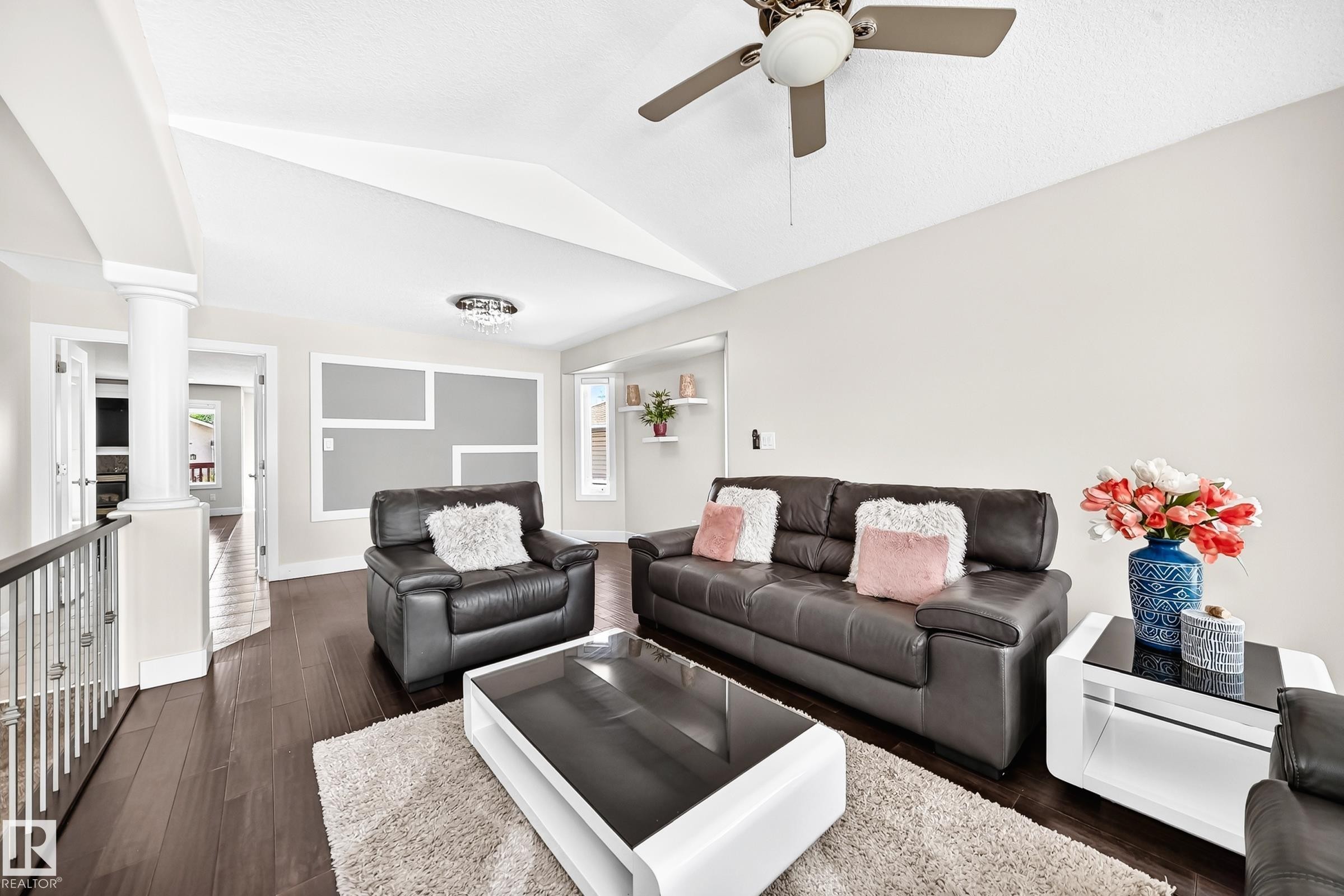 Spacious living area featuring vaulted ceilings, dark wood-finish flooring, a decorative accent wall, a ceiling fan, and built-in shelving - 16124 76 Street, Edmonton, AB