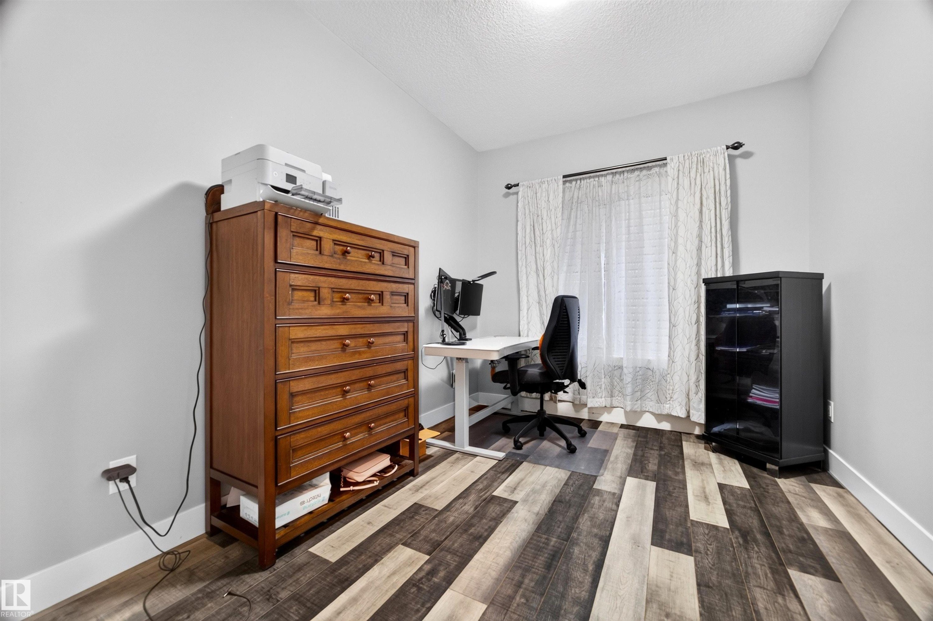 Room featuring two-tone wood-finish flooring, light gray wall paint, and a window with white blinds and sheer curtains - 1603 158 Street, Edmonton, AB