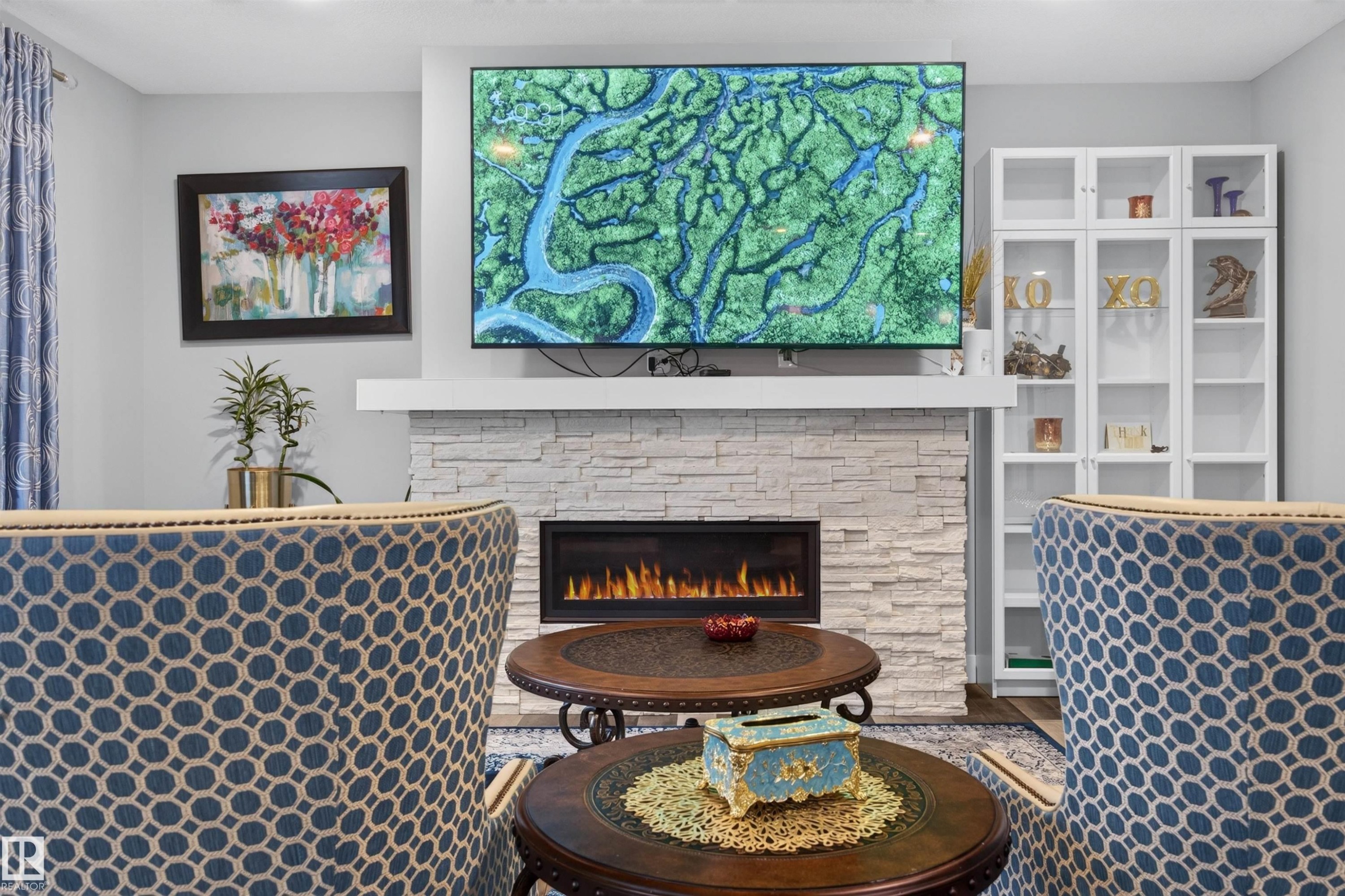 Living area featuring a floor-to-ceiling stacked stone fireplace with an integrated electric firebox, a white mantel, and built-in shelving with glass doors - 1603 158 Street, Edmonton, AB
