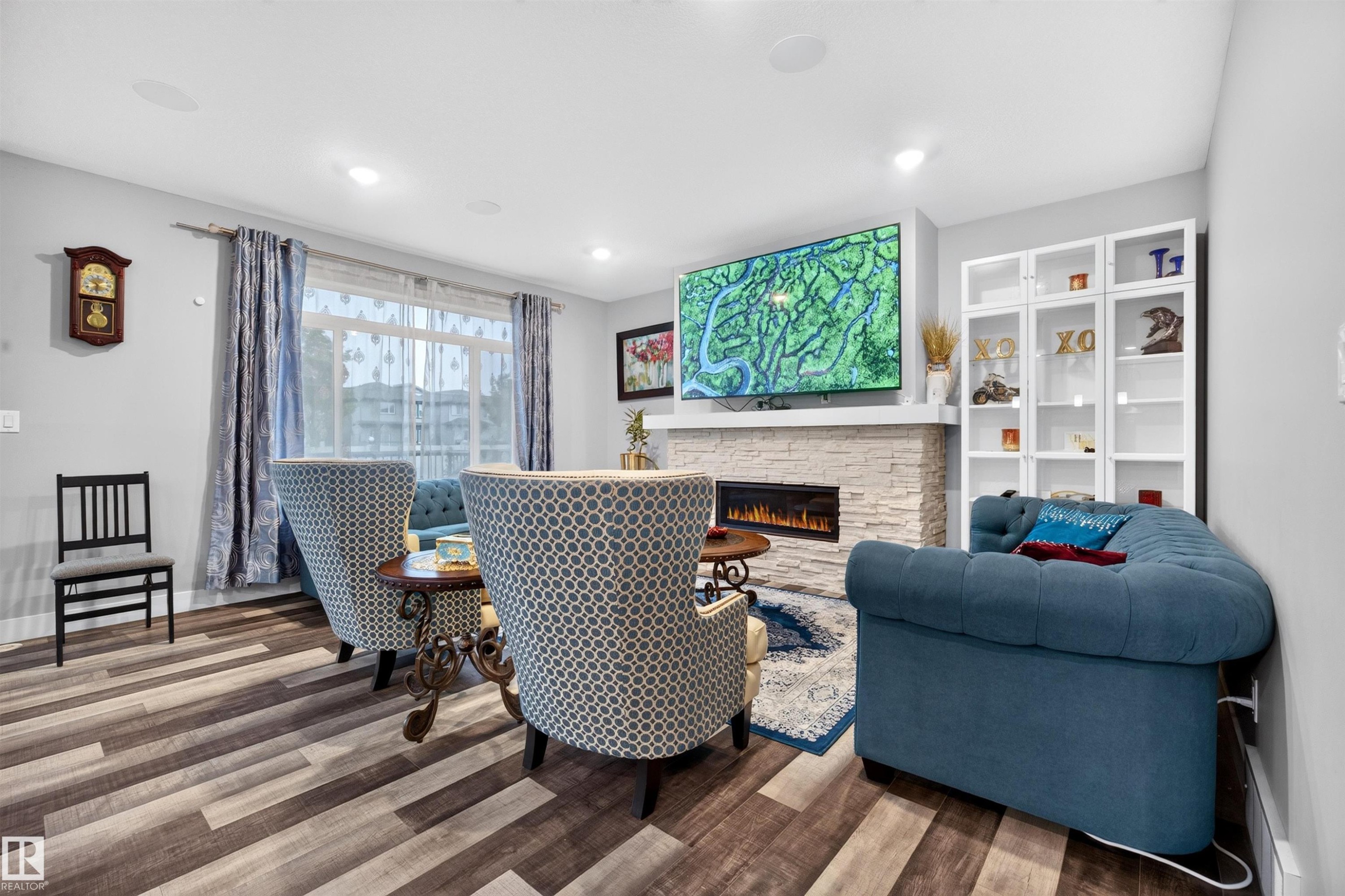 Living space featuring wood-finish flooring, recessed lighting, and a linear electric fireplace with a stacked stone surround - 1603 158 Street, Edmonton, AB
