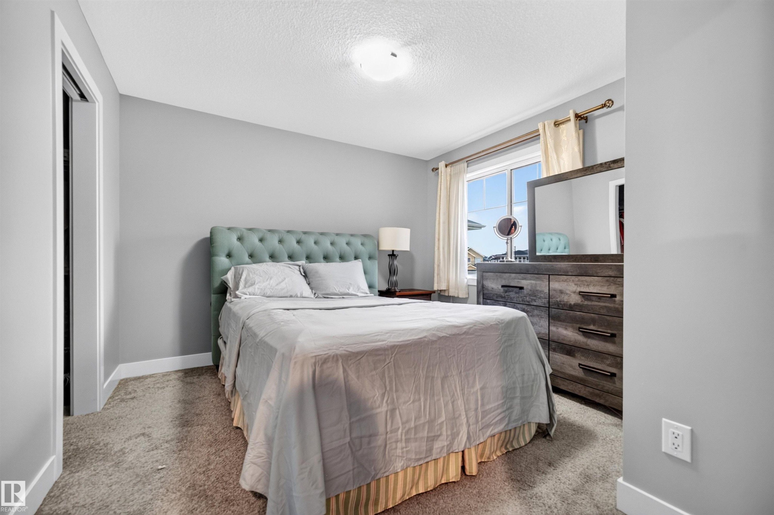 Carpeted bedroom with a window, white trim, and a built-in closet with bifold doors - 1603 158 Street, Edmonton, AB