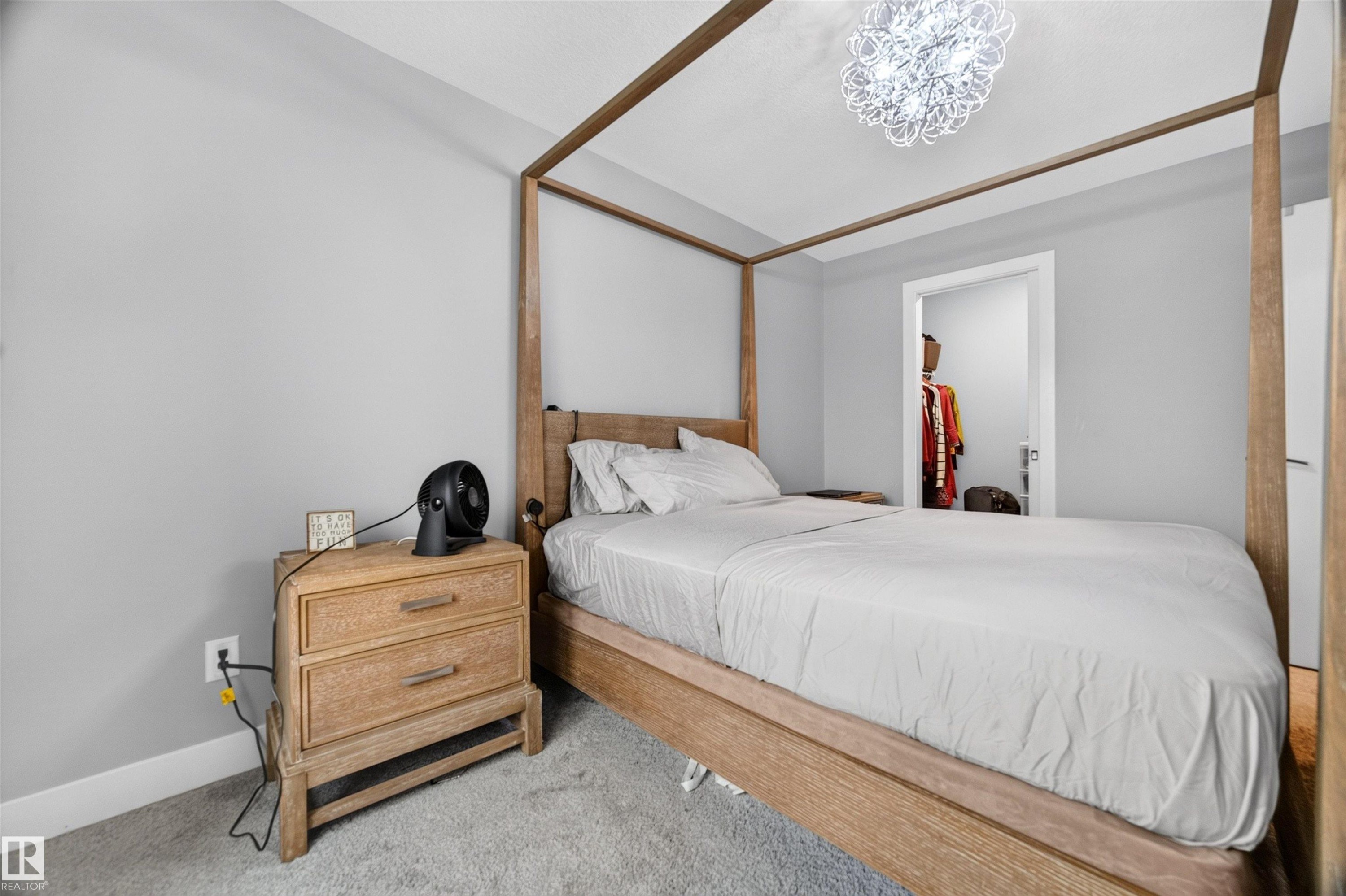 Carpeted bedroom featuring light gray walls, a contemporary chandelier, and an open doorway leading to a closet space - 1603 158 Street, Edmonton, AB