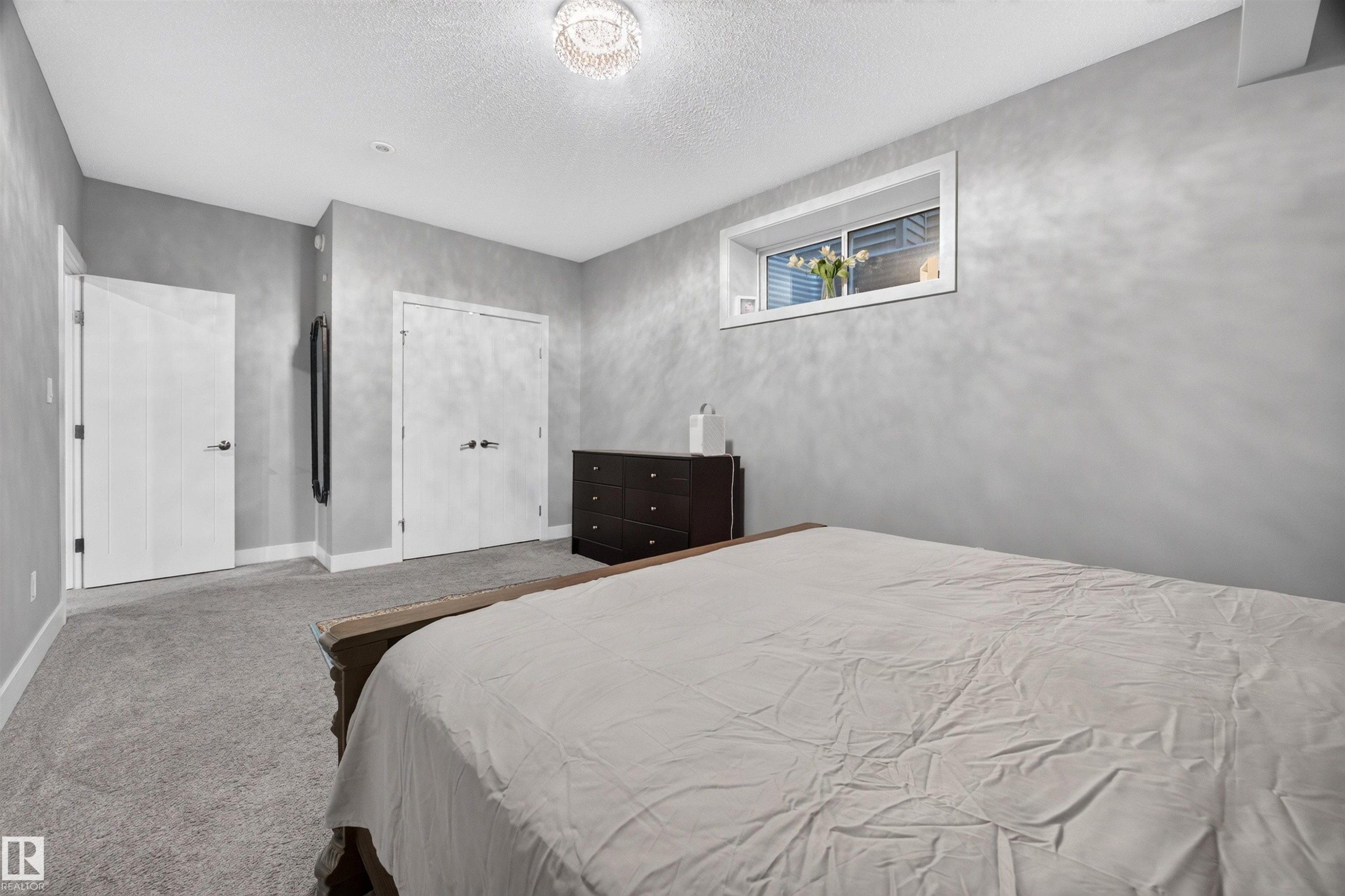 Spacious room with light gray walls, plush gray carpet, a white trim window, a modern ceiling light fixture, and two white panel doors - 1603 158 Street, Edmonton, AB