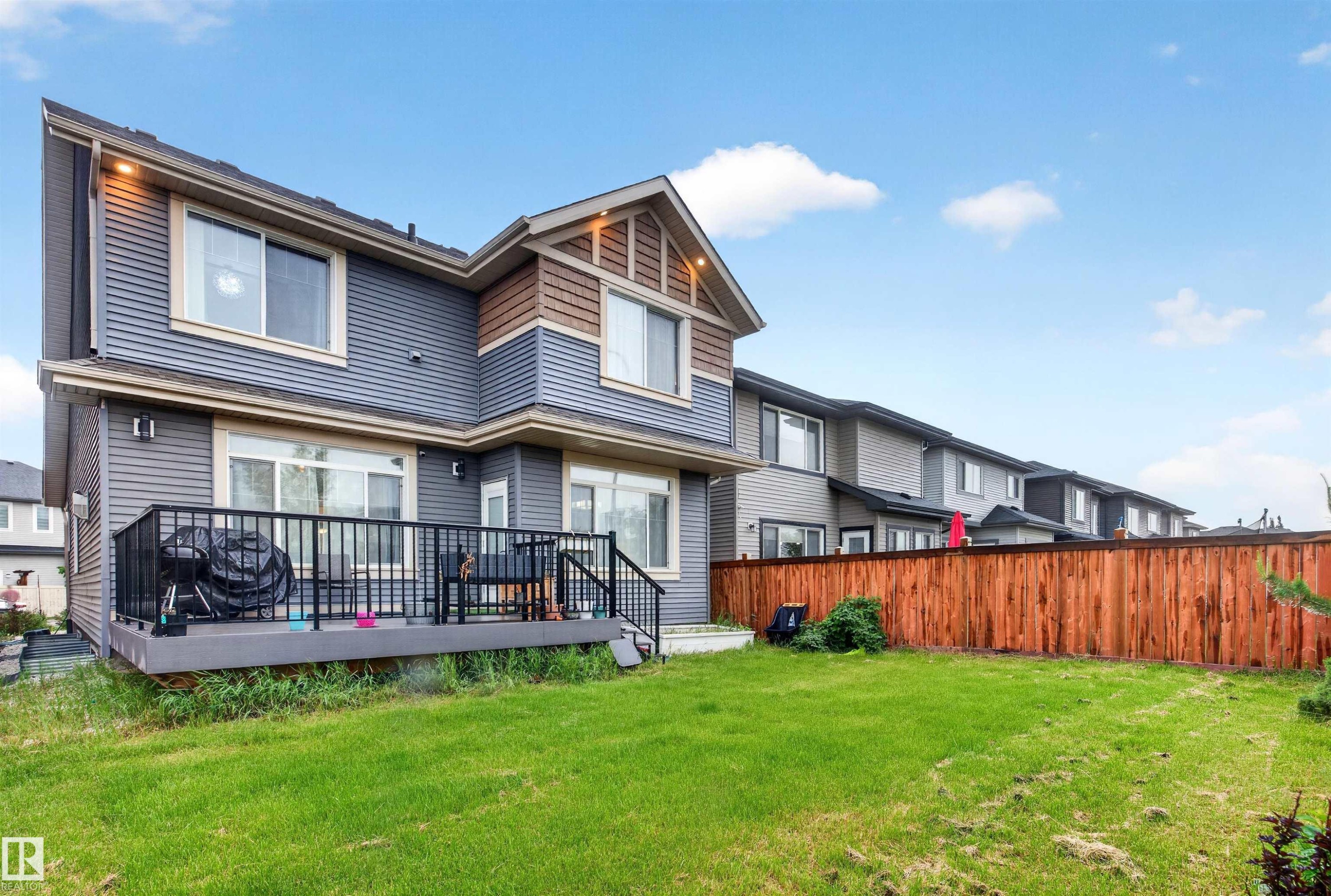 Expansive green lawn with a two-story residence featuring horizontal siding, a private deck with black railing, and a wood privacy fence - 1603 158 Street, Edmonton, AB