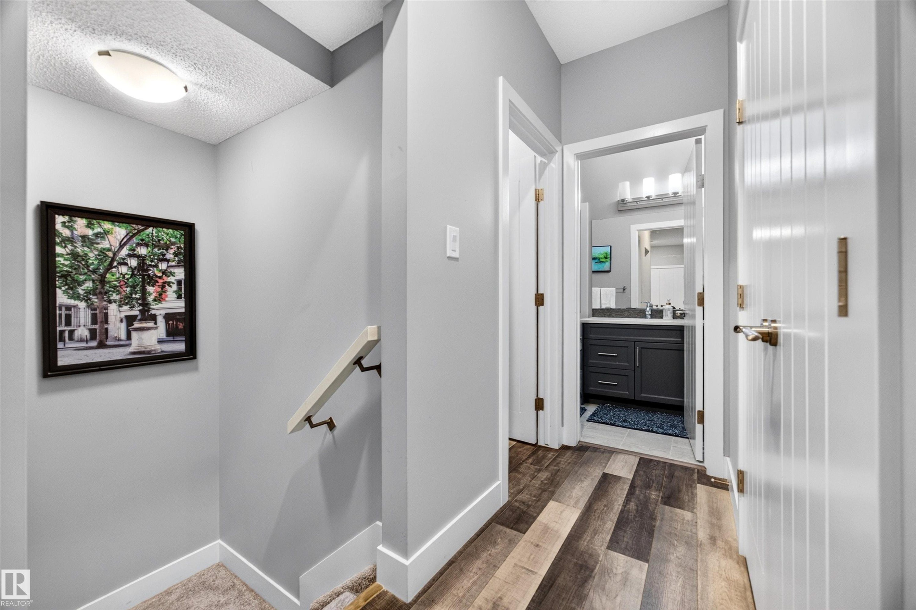 Hallway with wood-finish flooring, light grey wall paint, and white baseboards - 1603 158 Street, Edmonton, AB