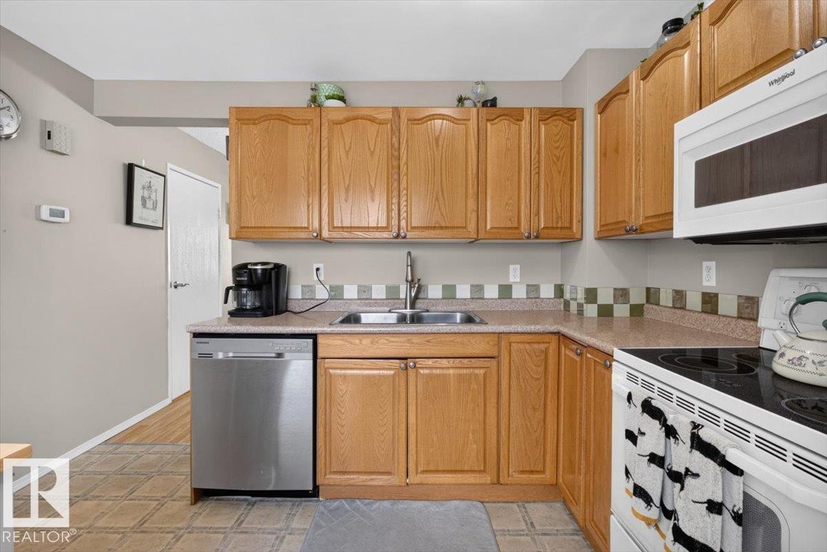 Kitchen featuring wood cabinetry, laminate countertops, stainless steel sink, tile backsplash, and stainless steel dishwasher - 27 Walden Park, St. Albert, AB