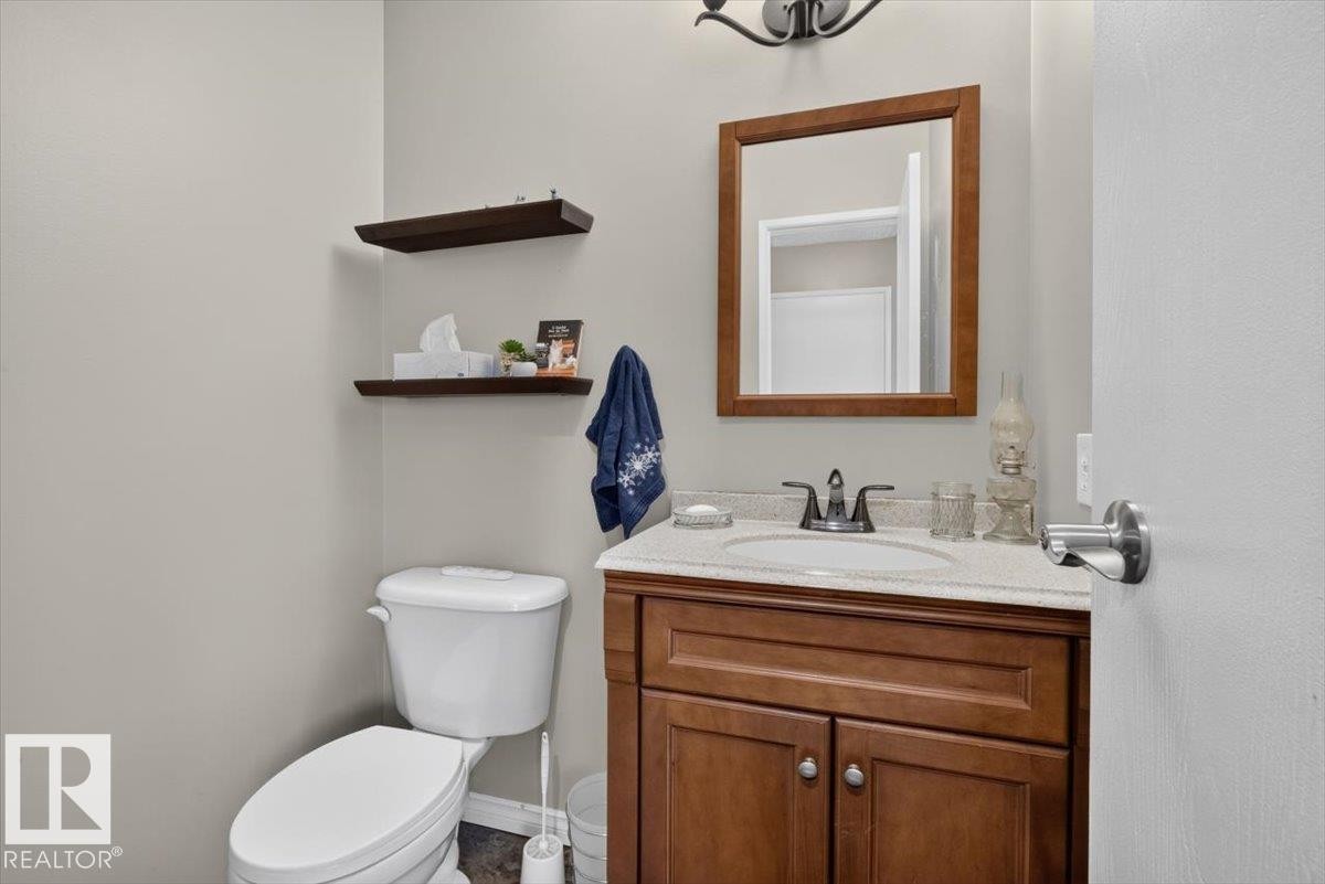 Powder room featuring a wood vanity with a white countertop and integrated sink, a wood-framed mirror, and two floating wood shelves - 27 Walden Park, St. Albert, AB